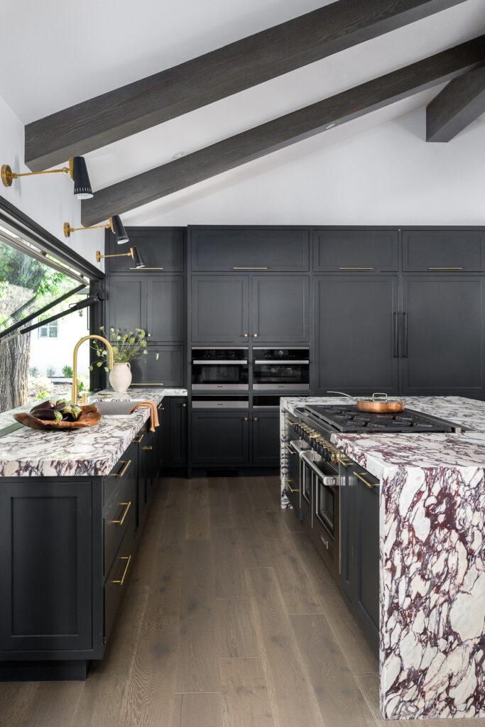 Dark and moody kitchen with black cabinets and marble waterfall counters