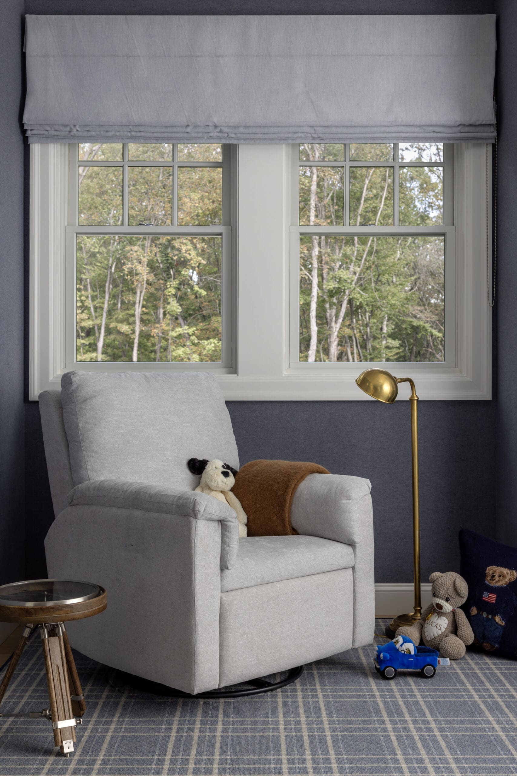 Cozy reading corner with a light gray armchair, plush toys, and a brass floor lamp by a large window.