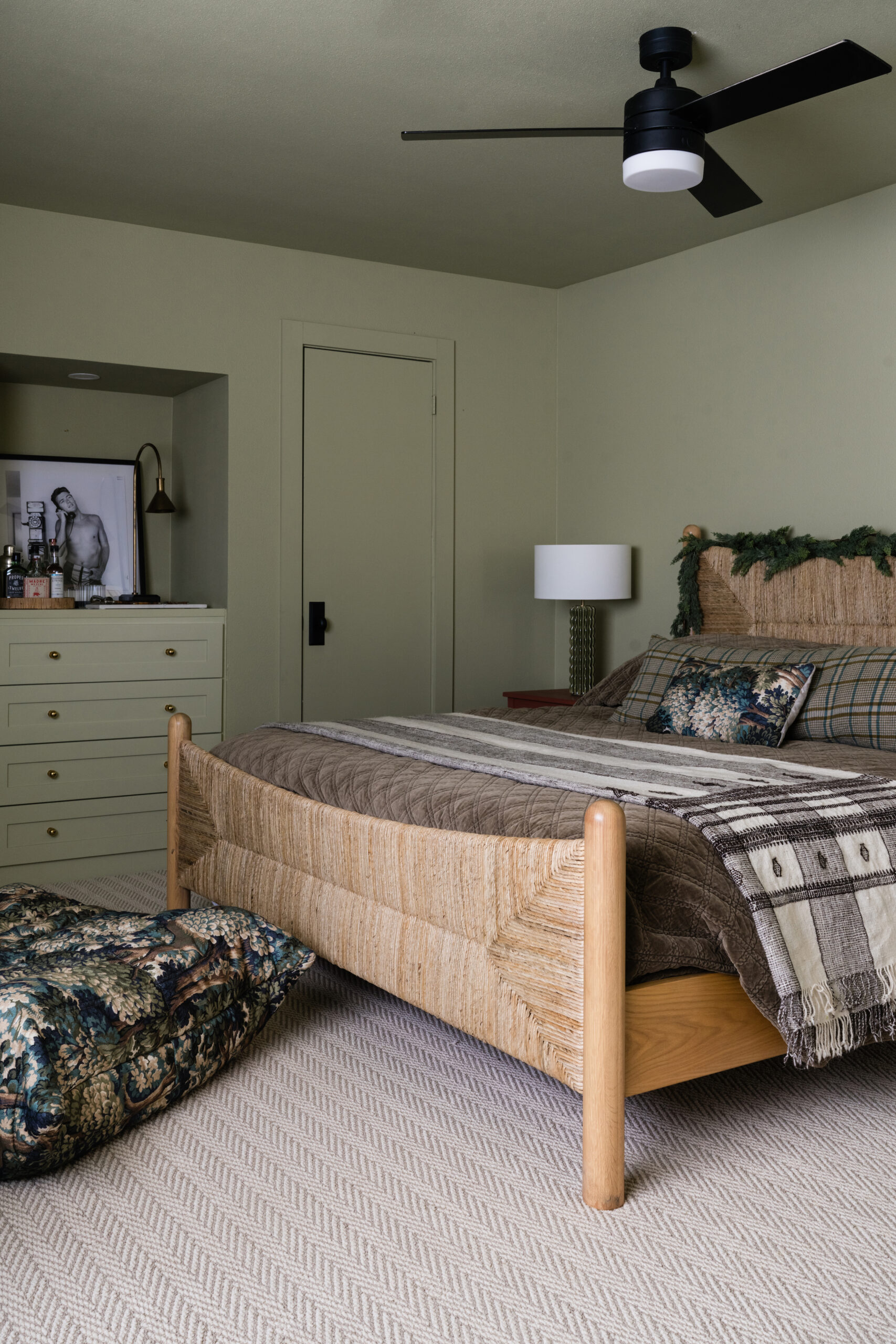 sage green bedroom with natural woven bed and holiday garland