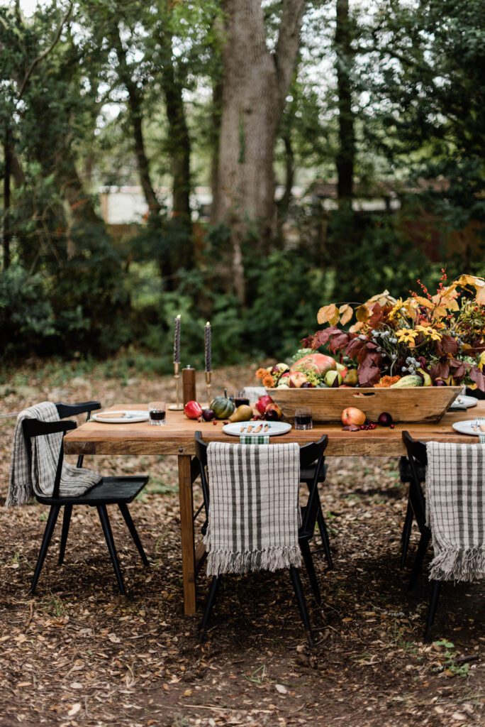 autumn harvest table with fall flowers , fruit and vegetable centerpiece and casual cozy blankets at each place setting
