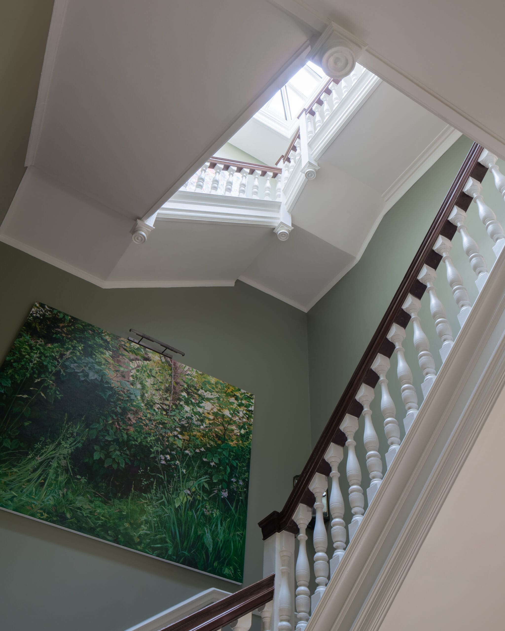 Interior staircase with white decorative balusters and dark wood handrail along a green wall; large jungle painting on the lower wall.