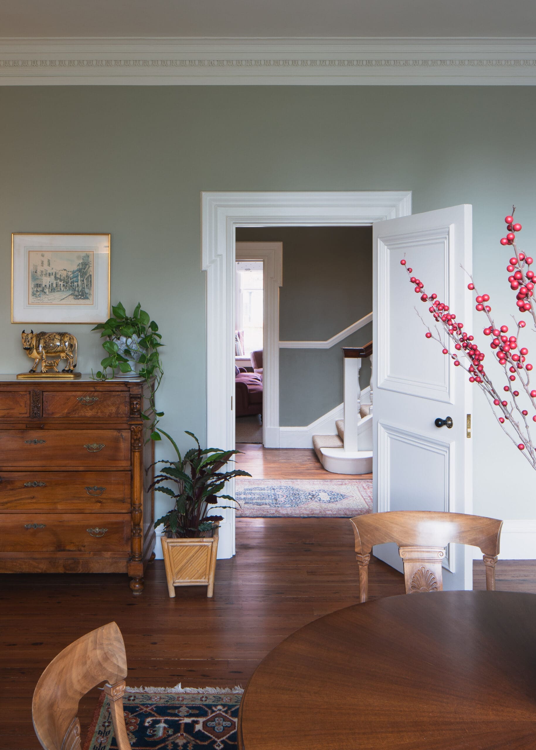 Living area with a green wall, white crown molding, a wooden dresser, potted plants, and an open doorway to the stairs.