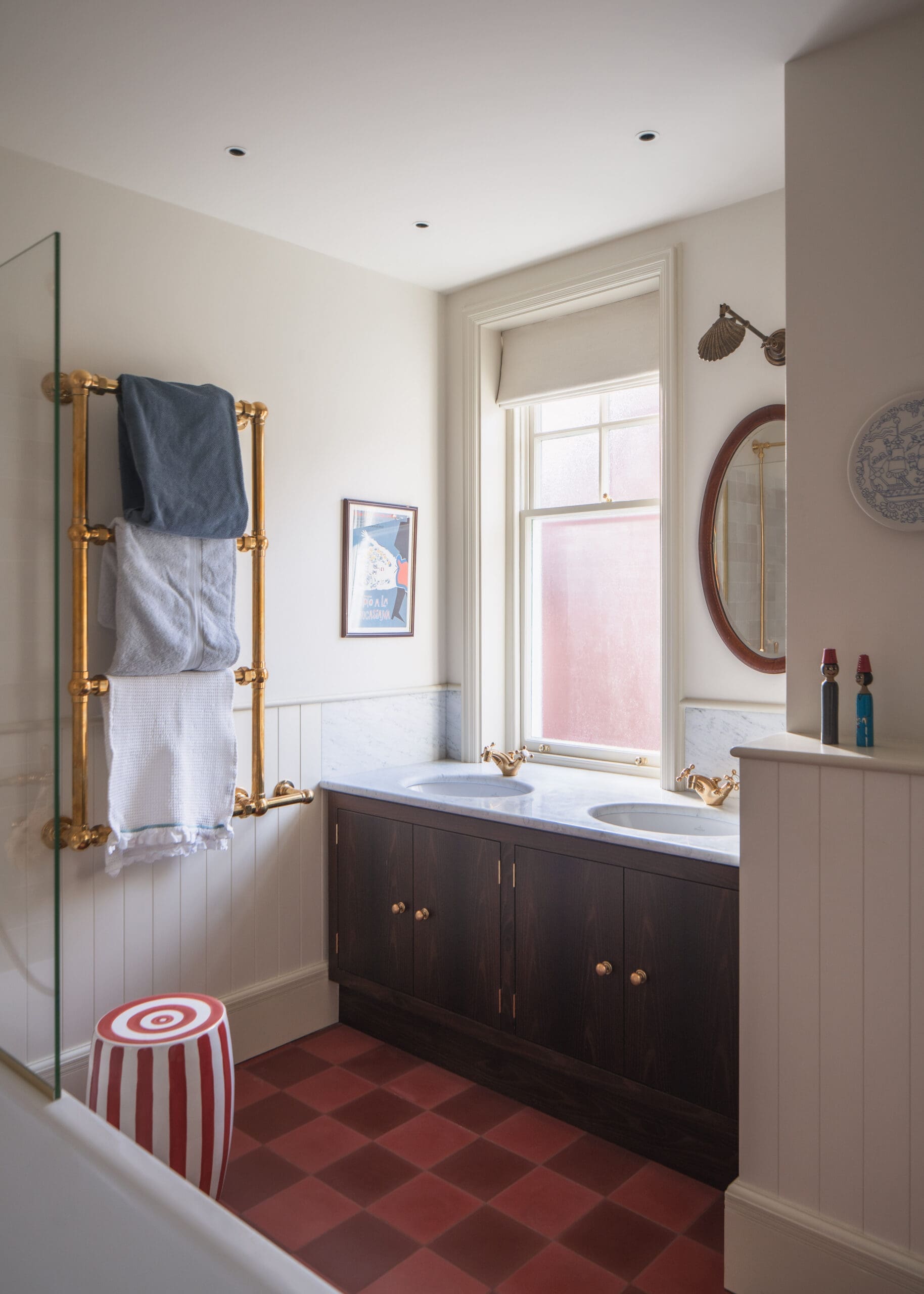 Bathroom with a dark wood double vanity, white marble tops, and gold fixtures beneath a large window.