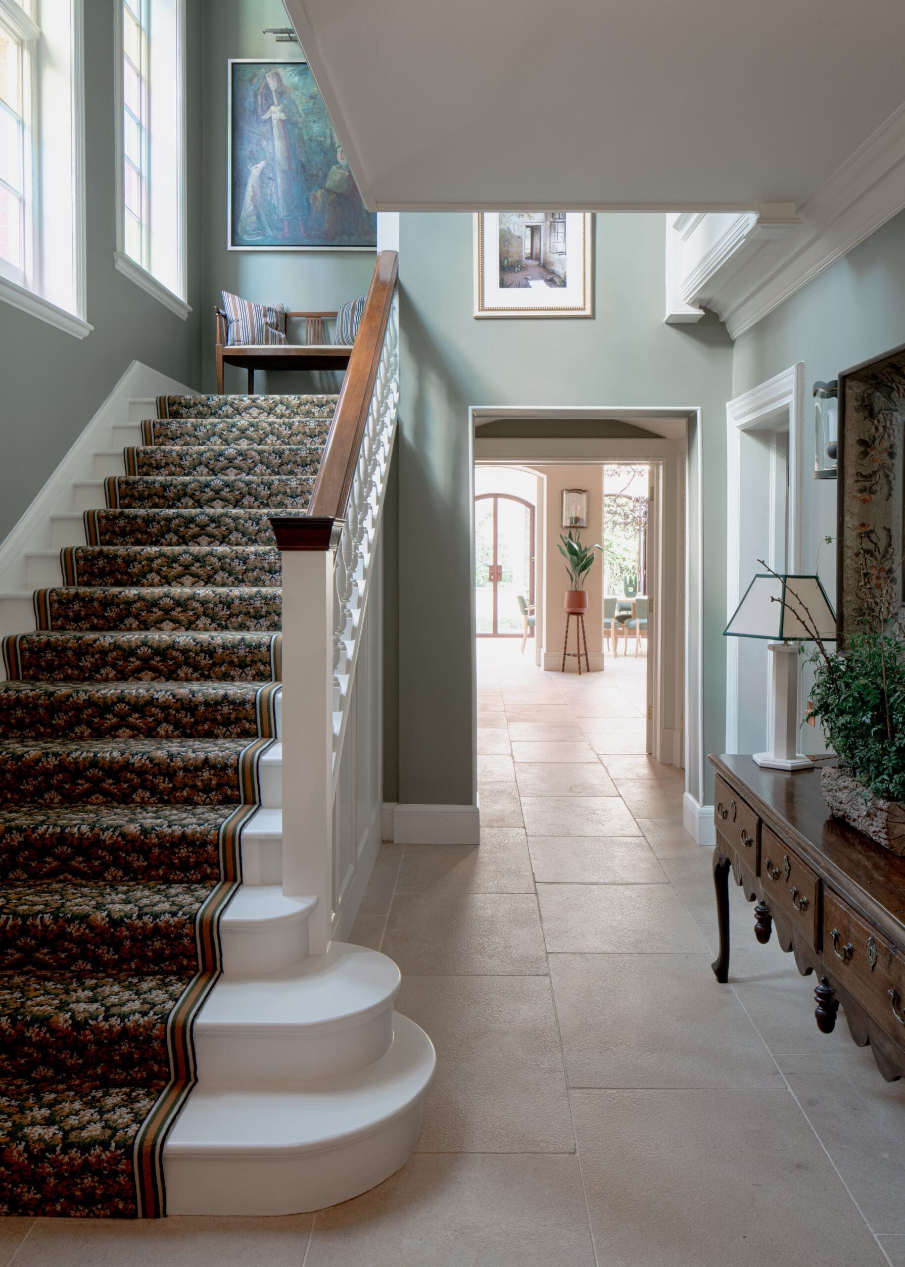 Elegant foyer with a carpeted staircase, mint walls, and a small seating nook on the landing.
