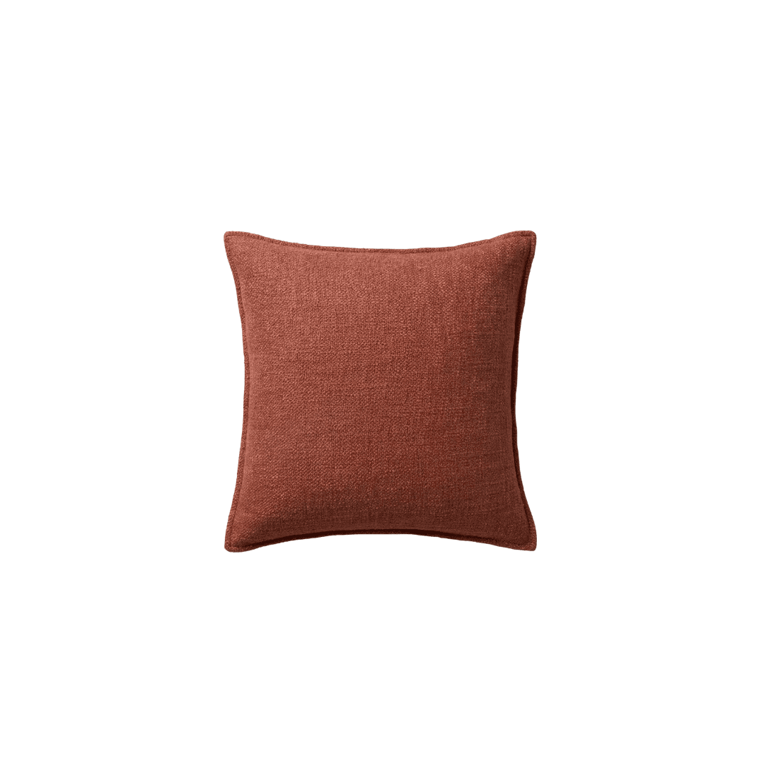 Rust-colored square throw pillow on a green background.