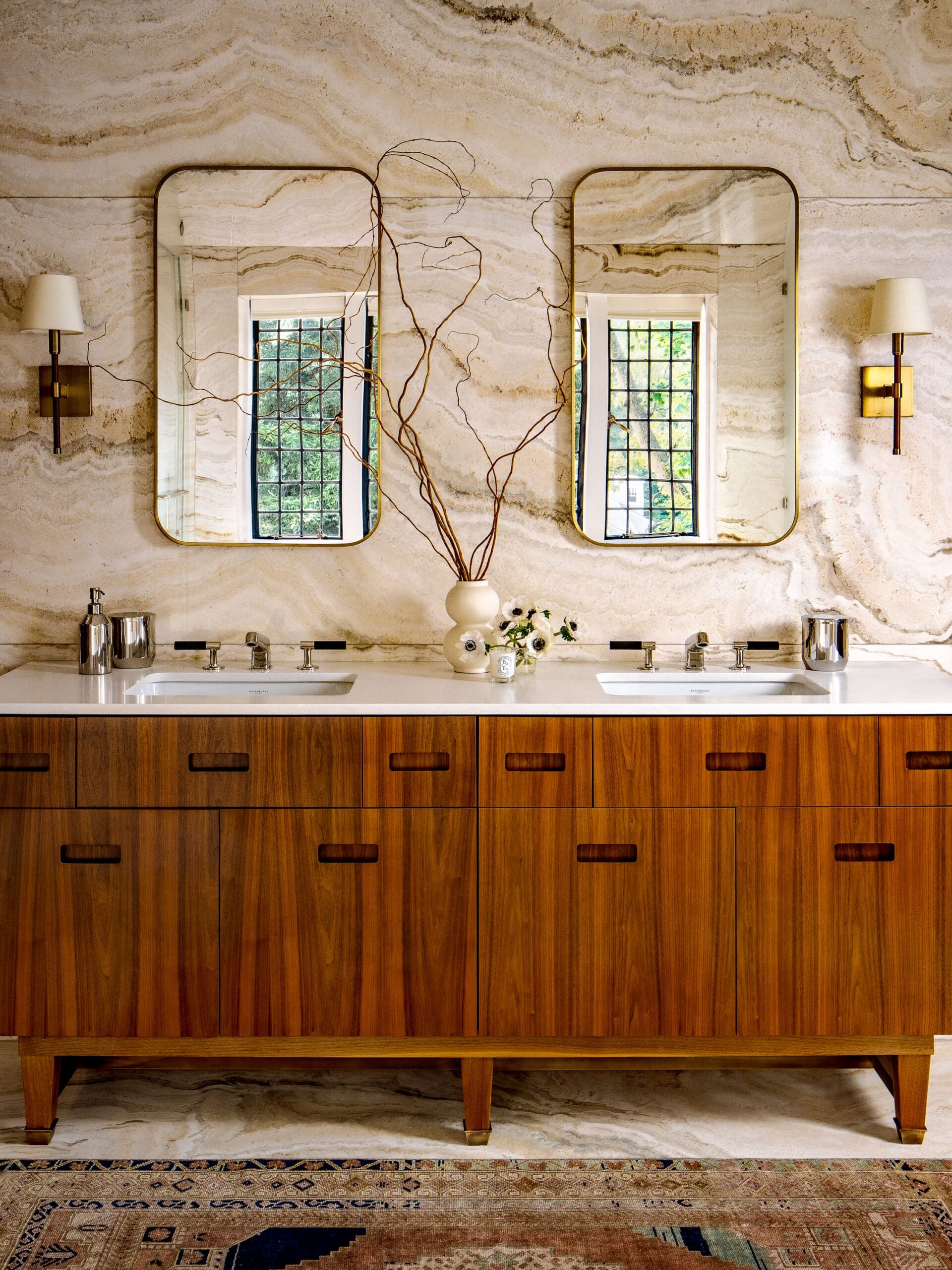 Double-sink bathroom vanity with mid-century wood cabinets, two rounded mirrors, and marble wall backdrop.