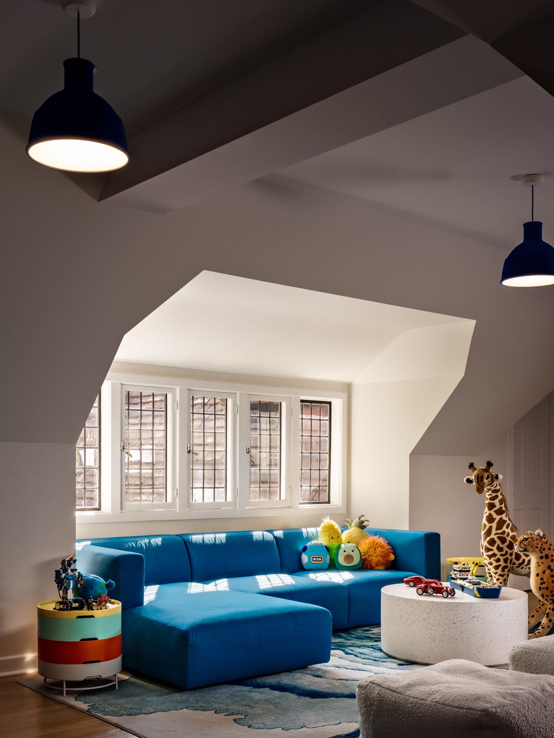 Colorful kids' playroom with a bright blue sectional sofa and stuffed animals by a windowed alcove.