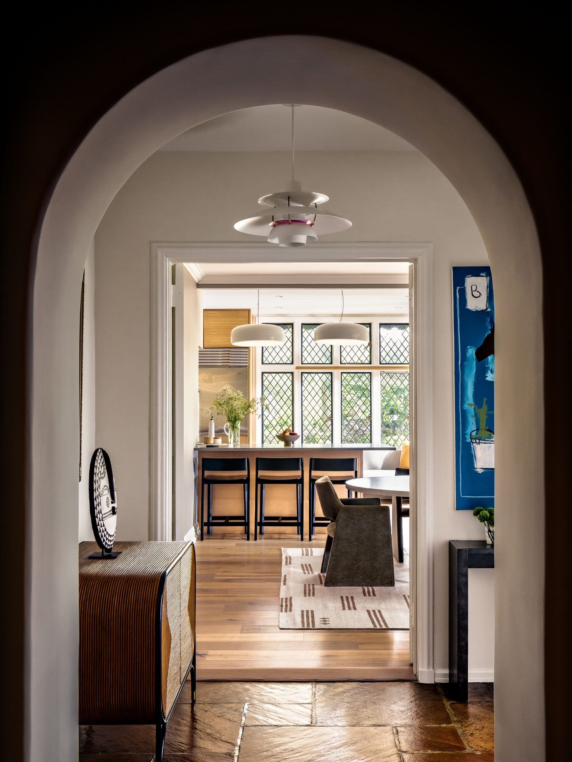Archway leads into a bright kitchen/dining area with a layered white pendant chandelier above a wooden counter and stools.