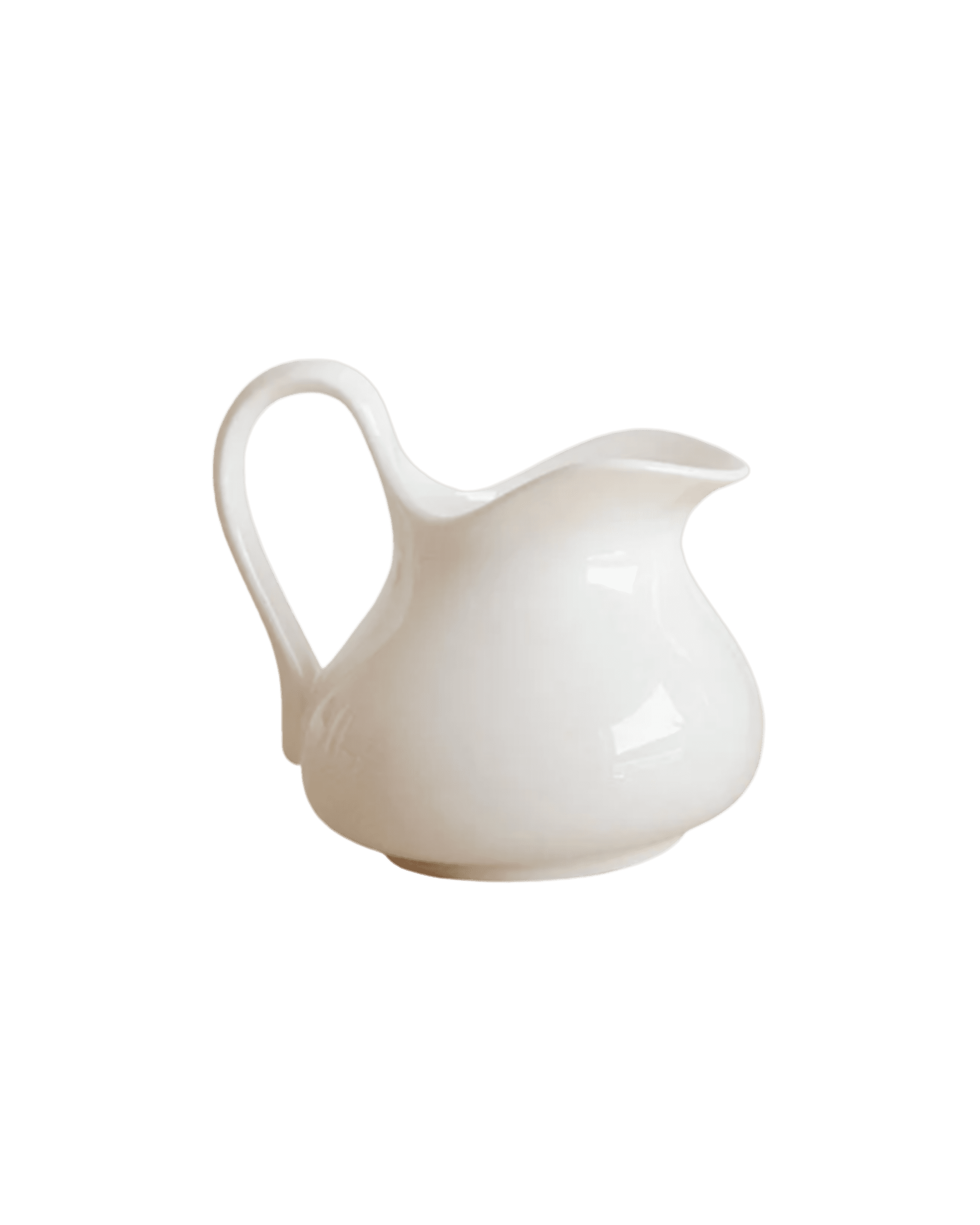 Partial view of a white ceramic pitcher with a rounded body, curved handle, and spout against a black background (creamer-style jug).
