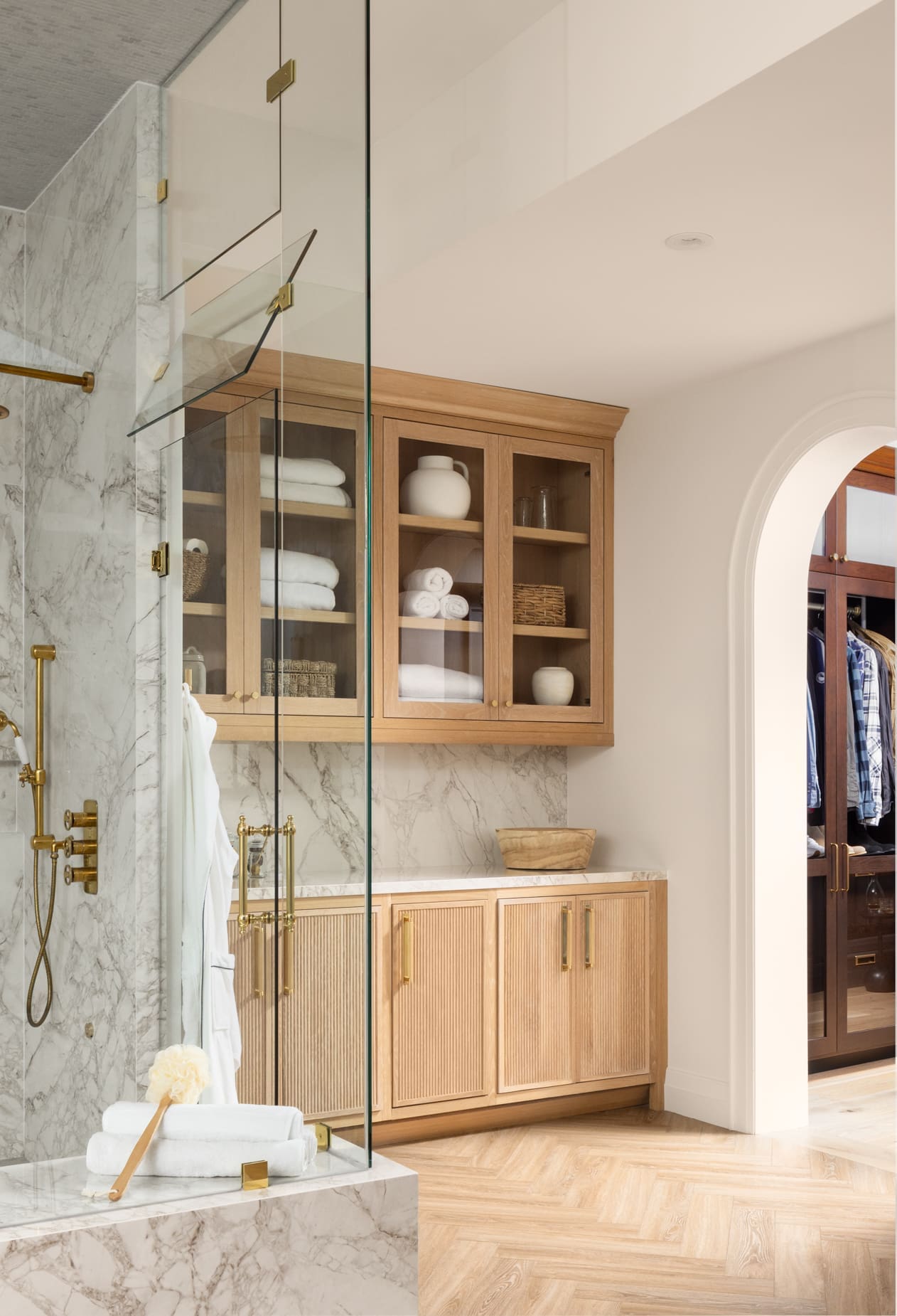 Luxurious bathroom with marble surfaces, glass shower enclosure, and oak cabinets displaying towels and decorative items.