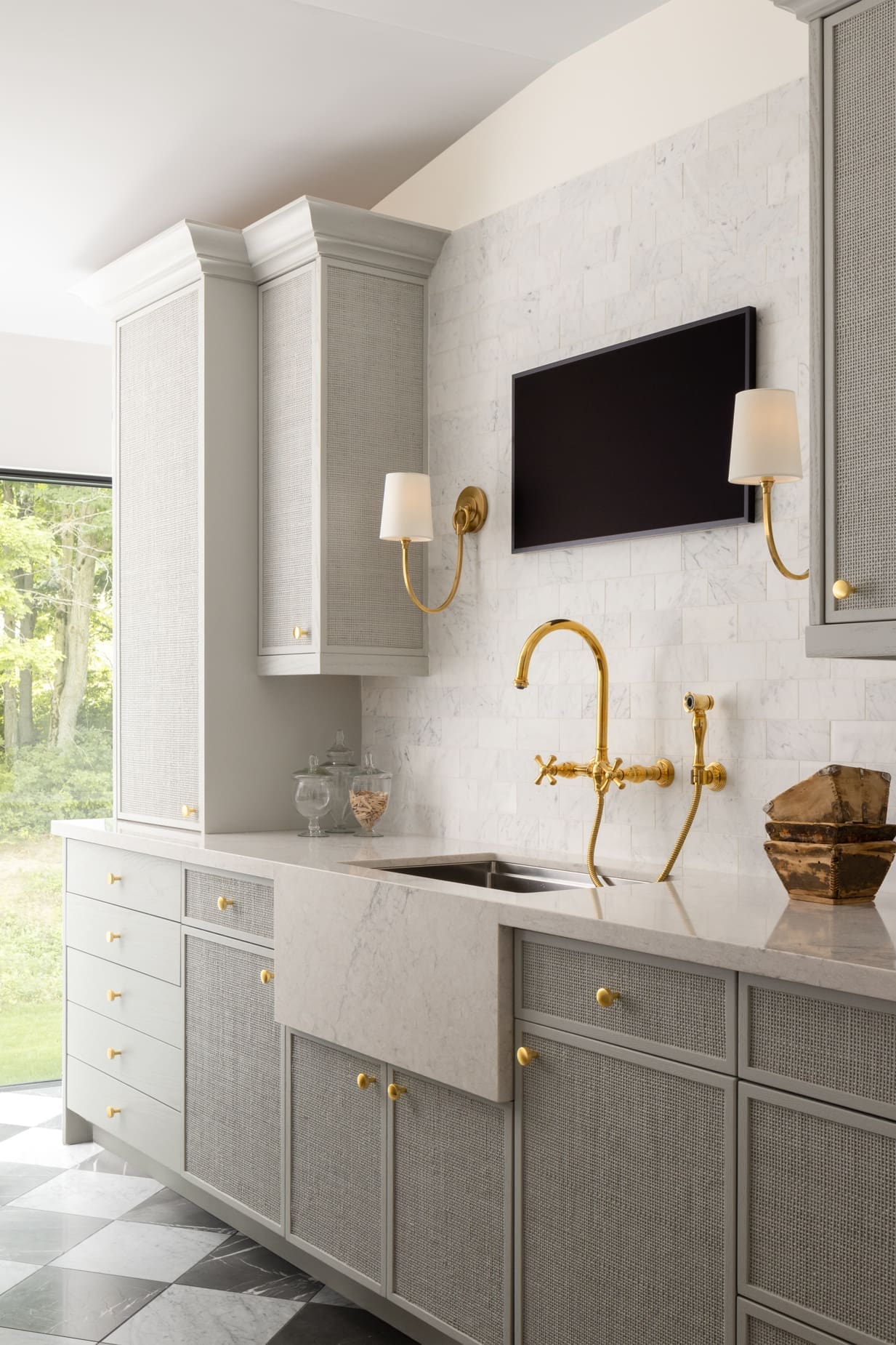 Luxurious galley-style kitchen with gray cabinets, gold faucet, and marble backsplash under a wall-mounted flat screen TV