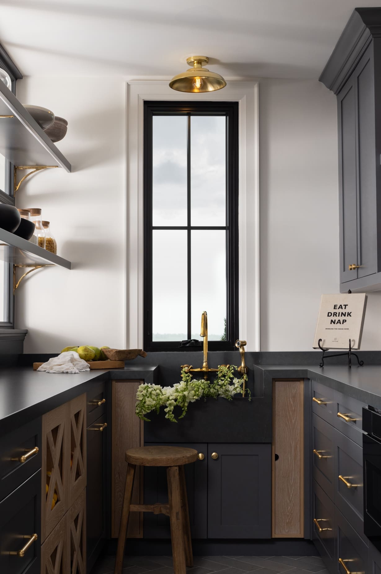 Modern kitchen with dark grey cabinets and brass hardware, open shelves, and a window above the sink.