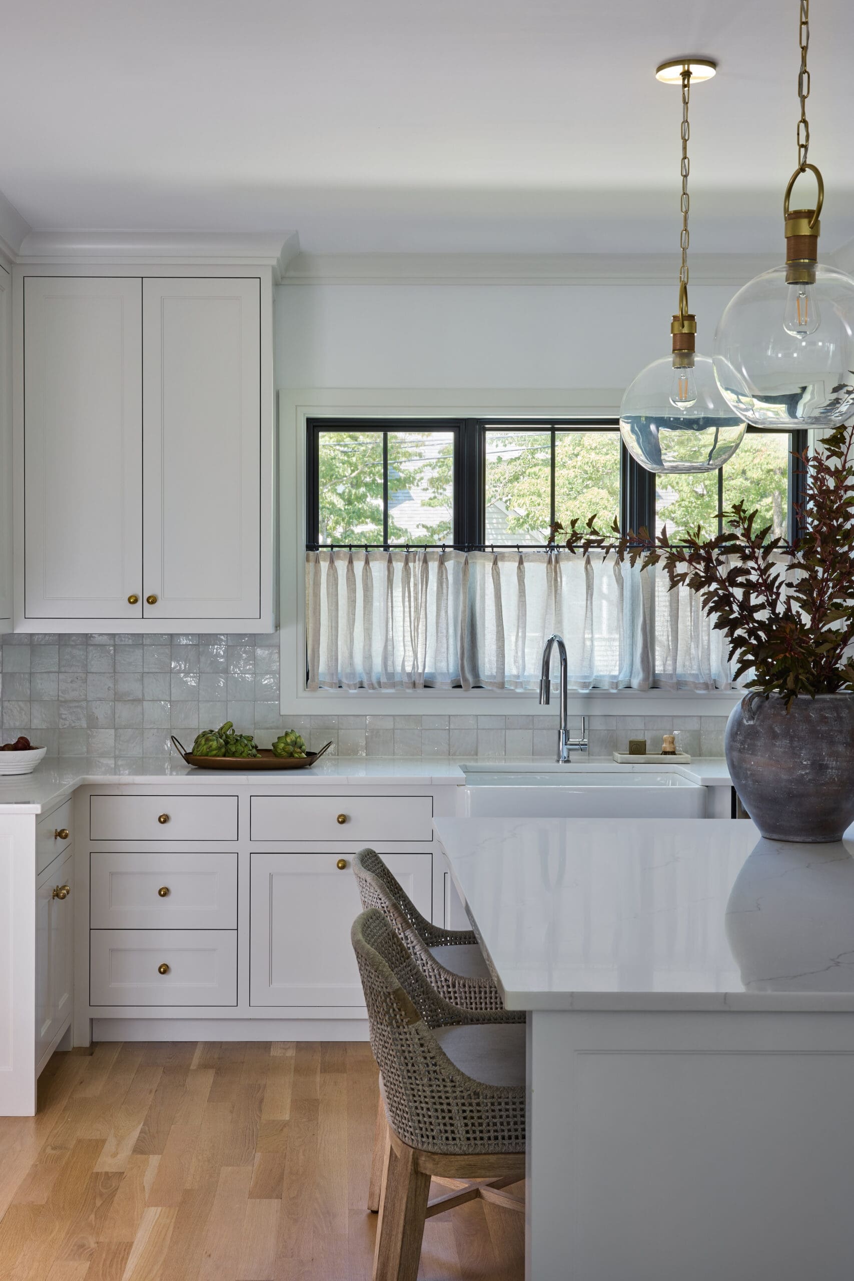 Bright white kitchen with shaker cabinets, brass knobs, and a white marble island beneath two hanging glass pendant lights.
