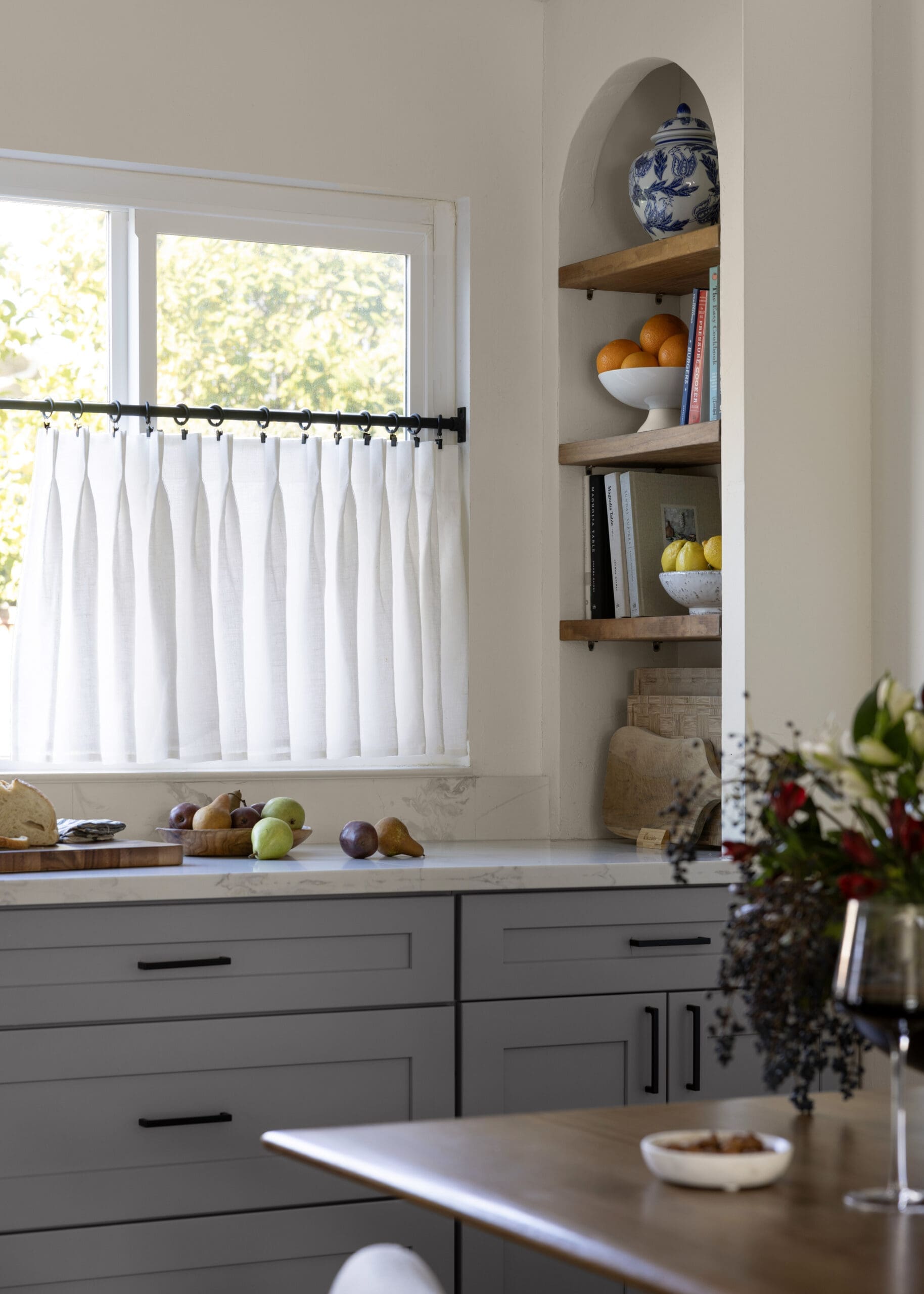 Kitchen counter with gray cabinets, white marble top, and an open shelving nook containing a blue-and-white jar and a bowl of oranges.