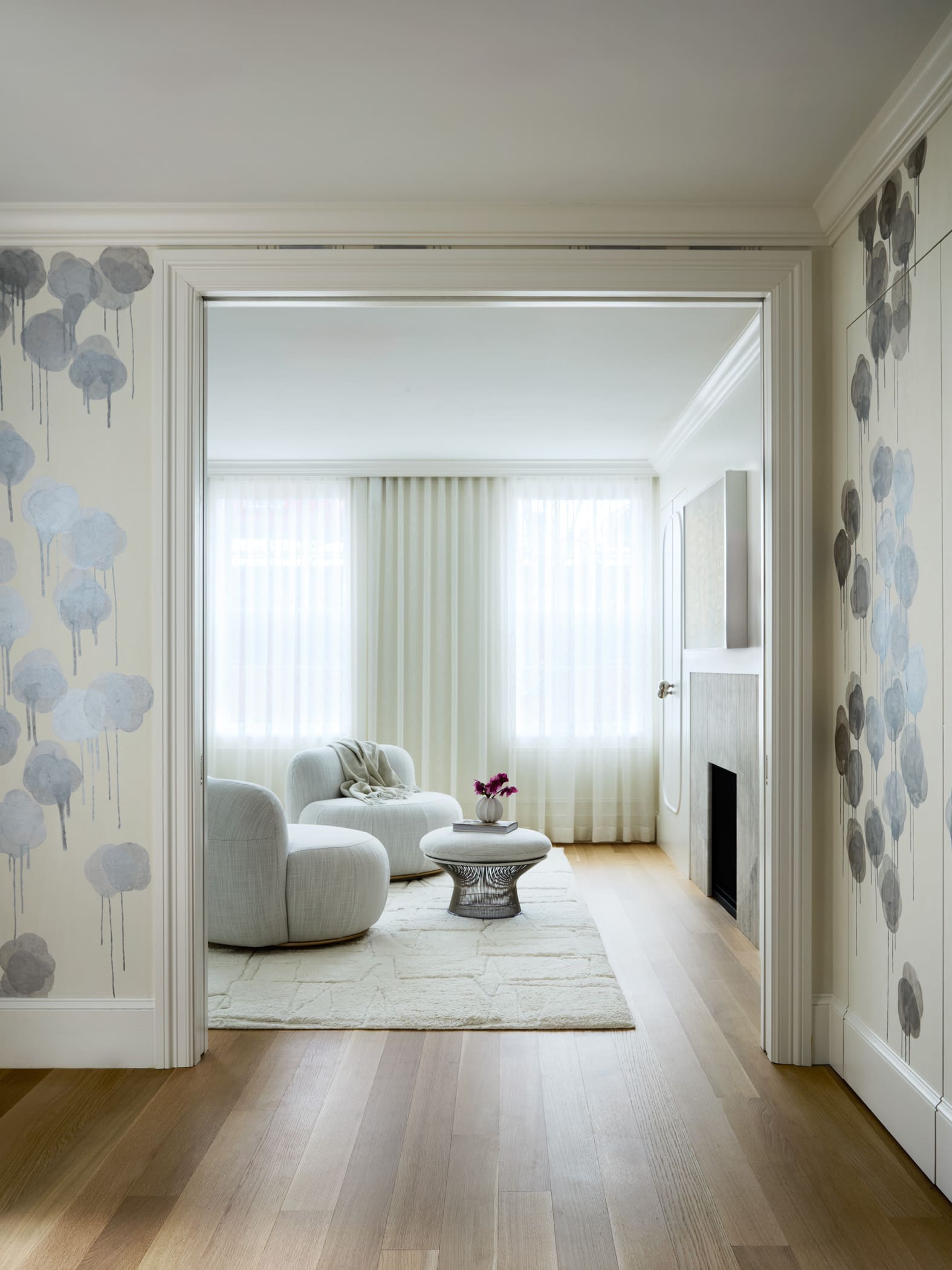 Bright living room with two curved gray chairs and a glass coffee table, seen through a doorway in a softly lit space.
