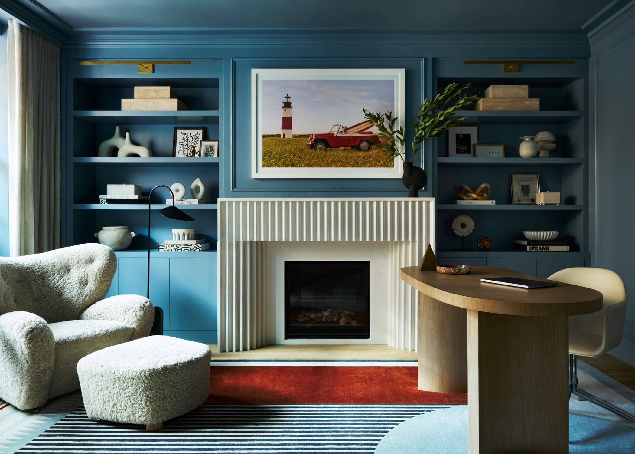 Blue built-in shelves surround a central framed photo of a lighthouse and red pickup in a stylish living room.