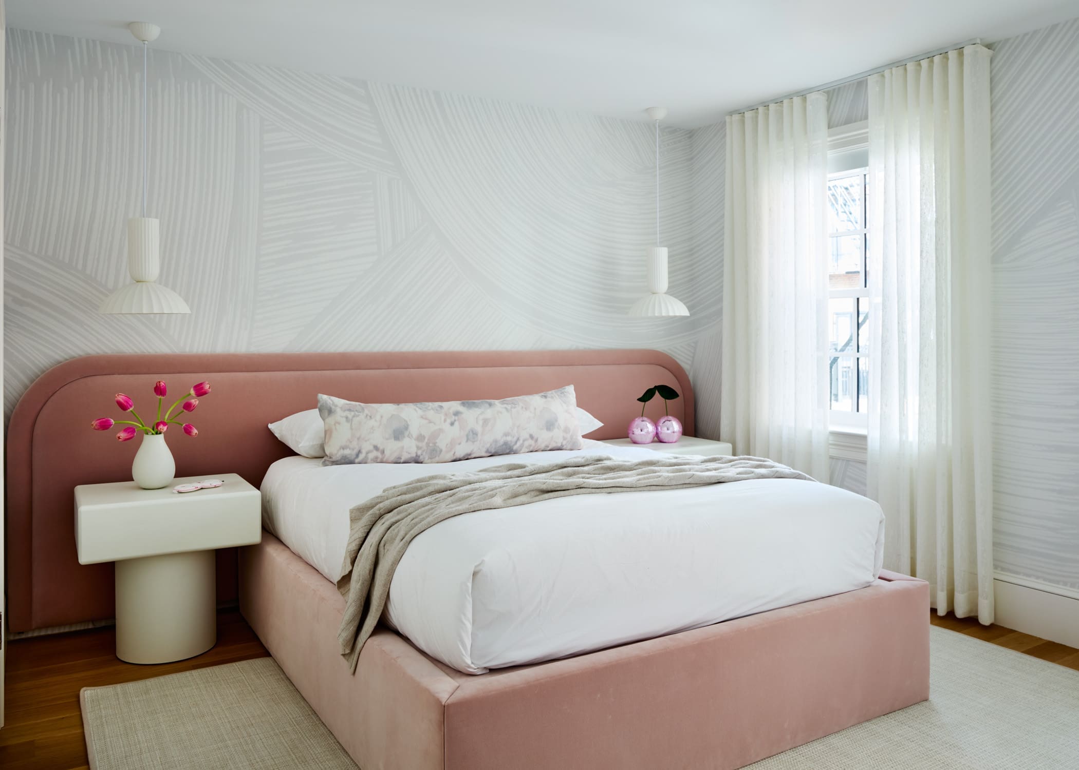 Bedroom with a pink upholstered bed, white bedding, and sheer curtains; modern pendant lights overhead.
