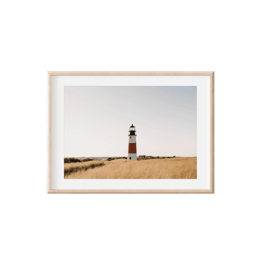 Framed photo of a red-and-white lighthouse in a golden grassy field under a pale sky.