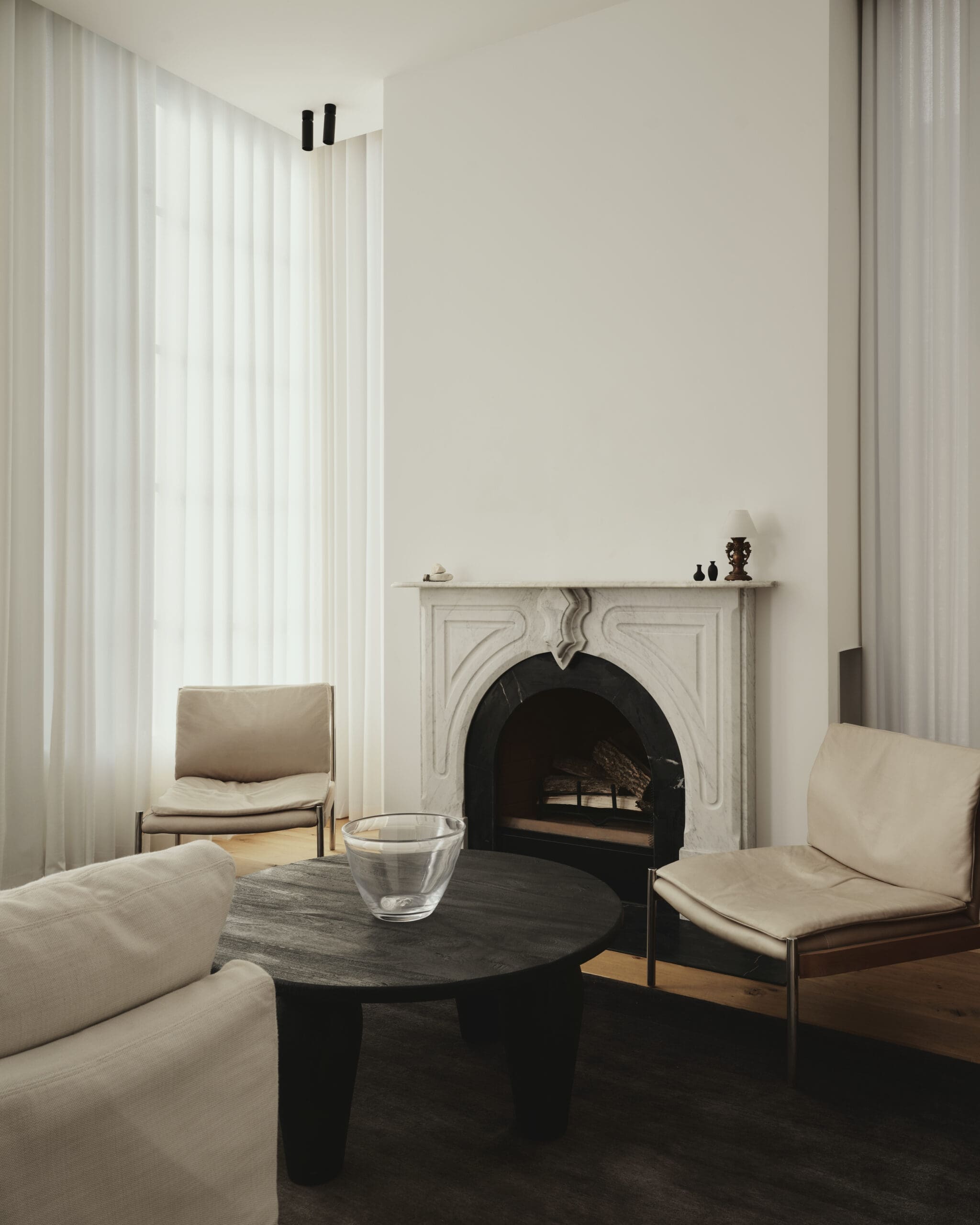 Living room with a marble fireplace, cream chairs, and a dark round coffee table holding a glass bowl.