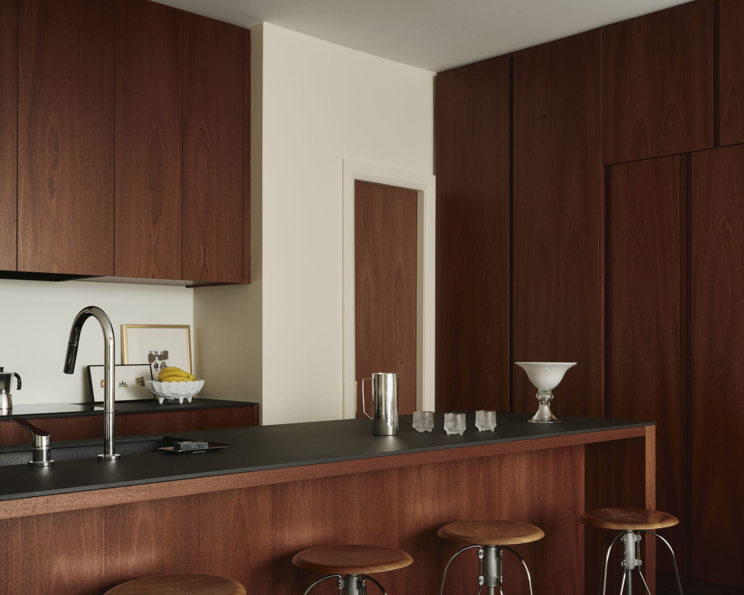 Modern kitchen with dark wood cabinets, black countertop, and bar seating; fruit bowl and glassware on the island.