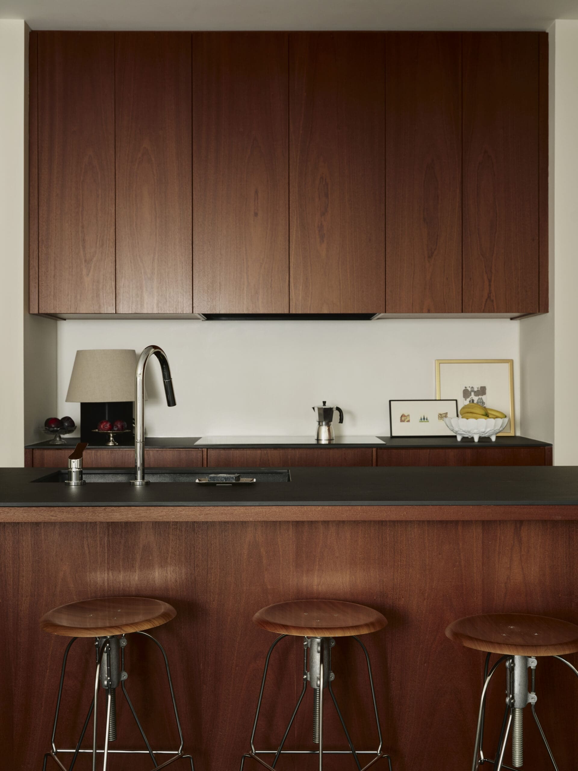 Kitchen with dark wood upper cabinets, black countertop, and three metal-bar stools in front of a bar-height counter.