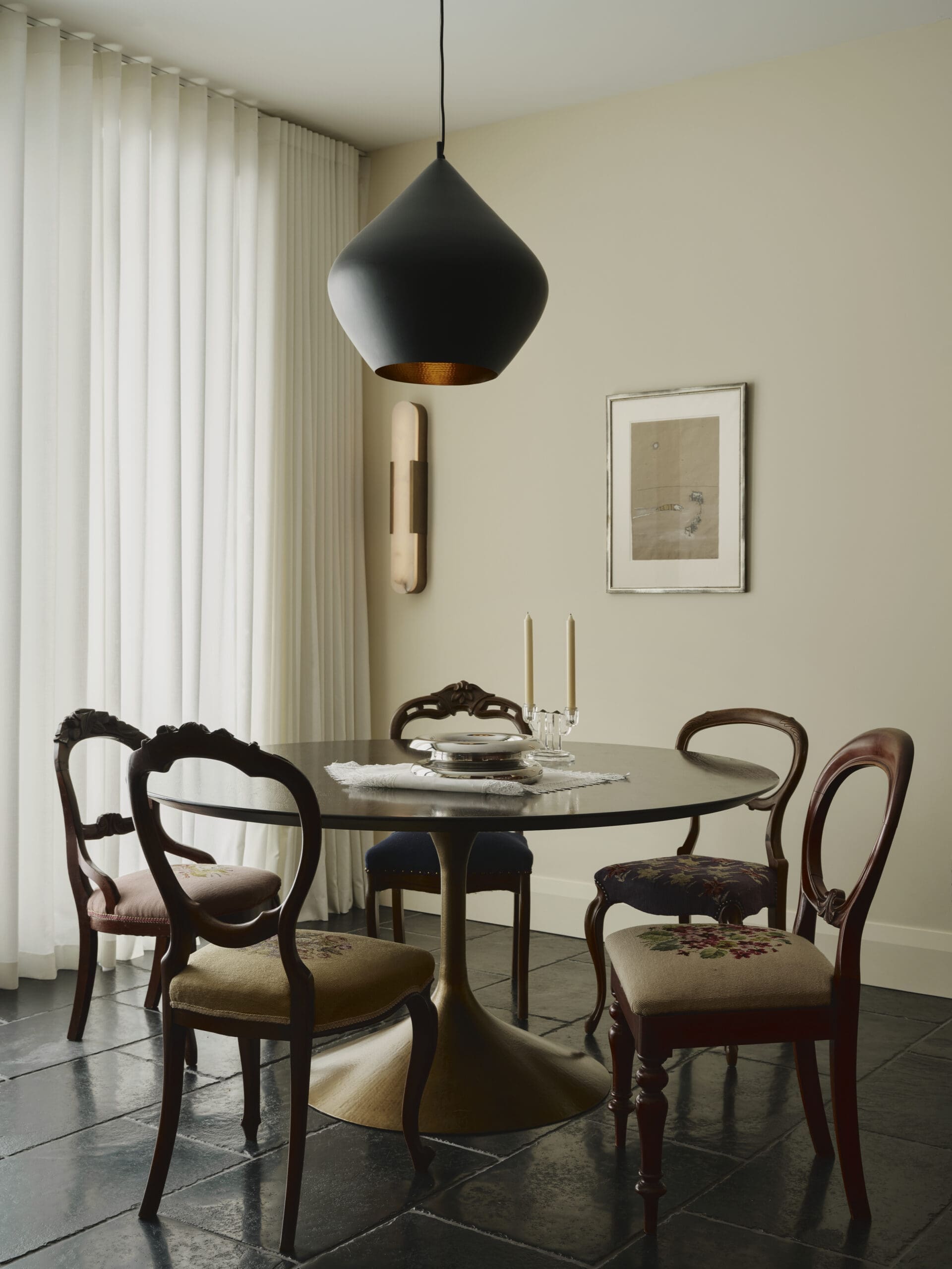 Round dining table with six carved wooden chairs in a beige dining room, a large black teardrop pendant light above.