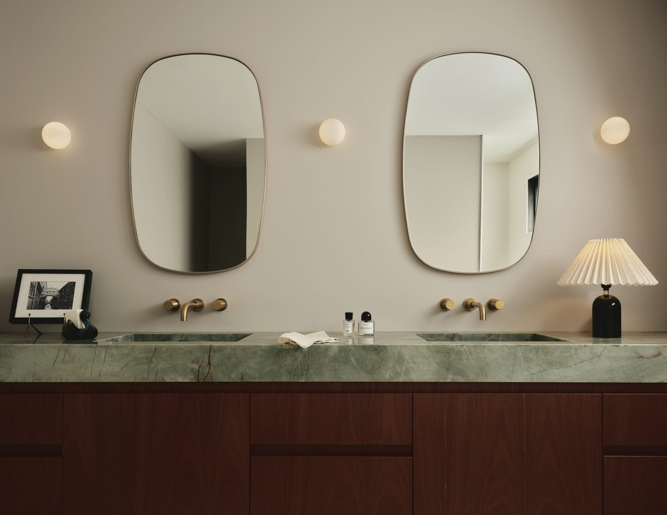 Double oval-mirrored bathroom vanity with warm wall sconces and a green marble countertop.