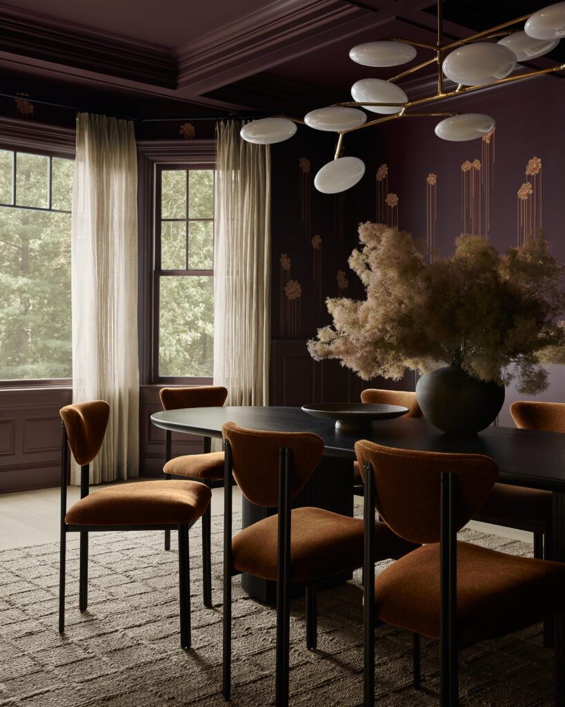 Elegant dining room with dark purple walls, gold-modern chandelier, and rust-colored chairs around a round table