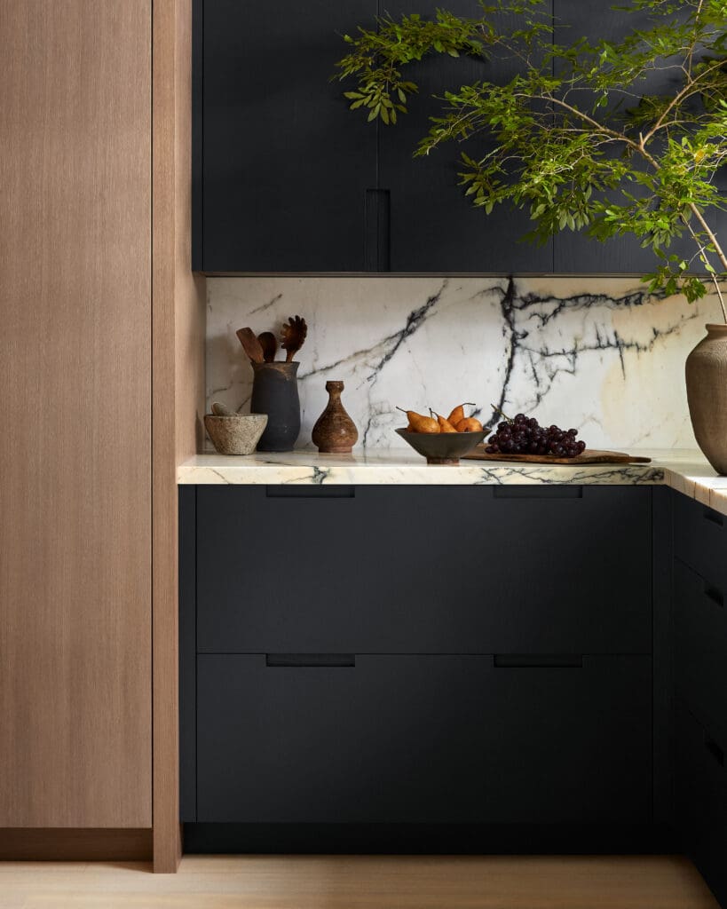 Modern kitchen scene featuring black lower cabinets, a white marble countertop with dark veining, and warm wood cabinetry framing the view.
