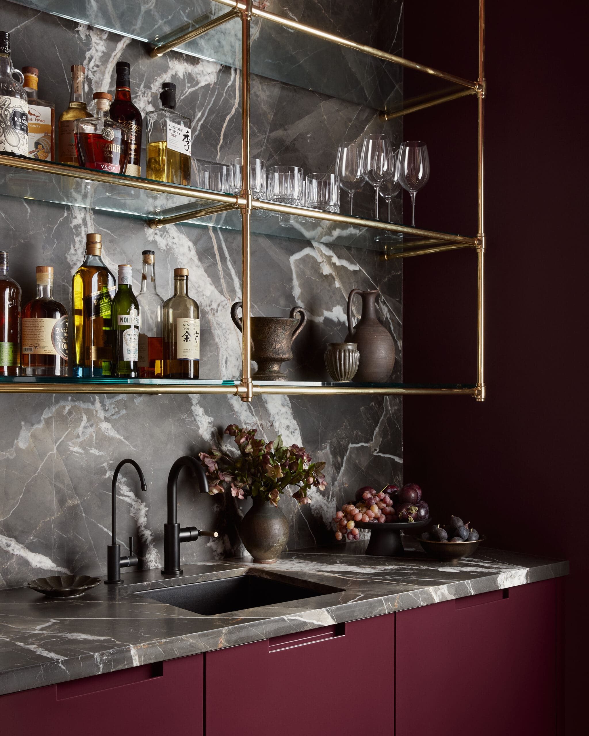 Marble and brass home bar with bottles on the top shelf and glassware on the middle shelf.