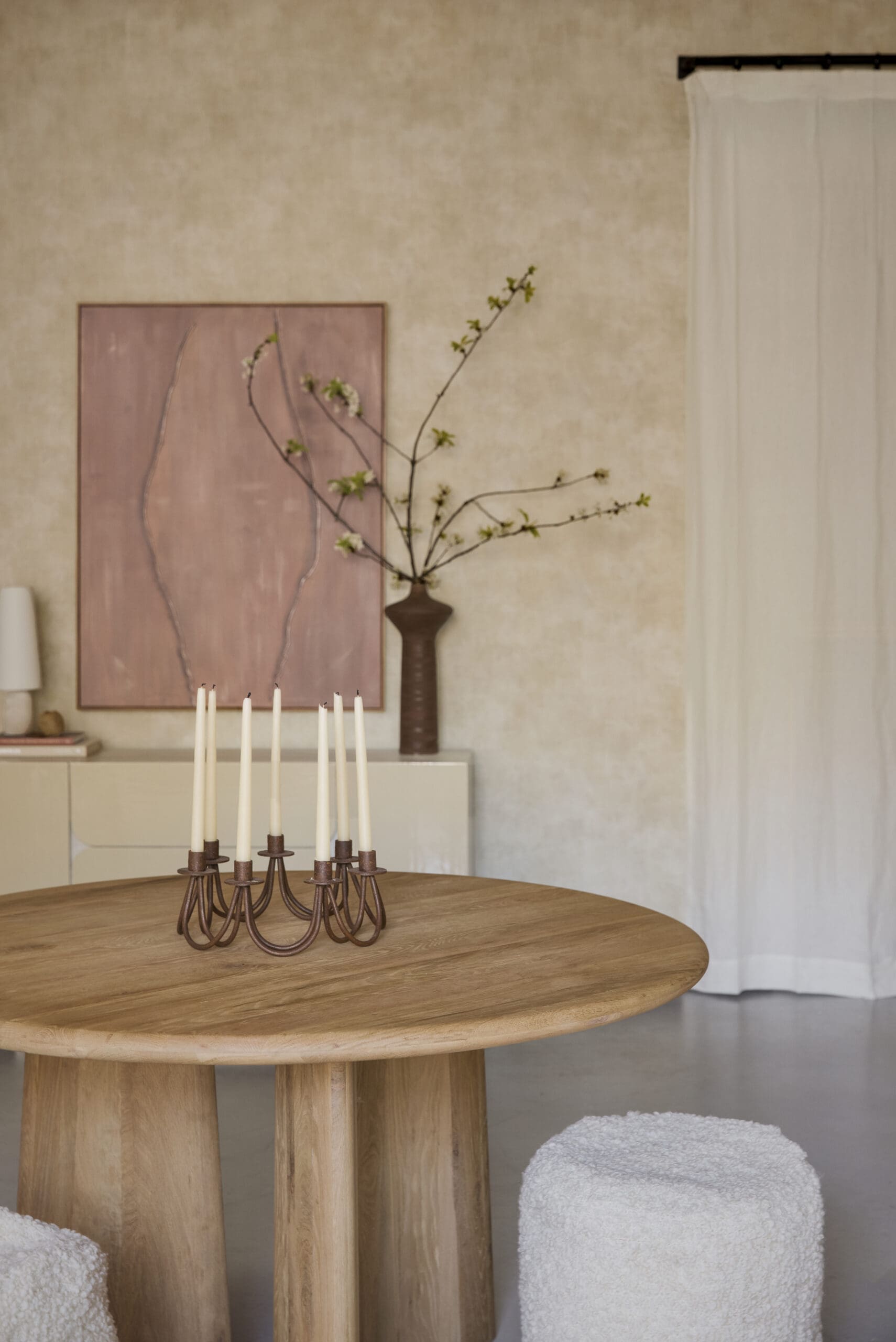 Round wooden dining table with a bronze candle holder and white taper candles in a warm beige room