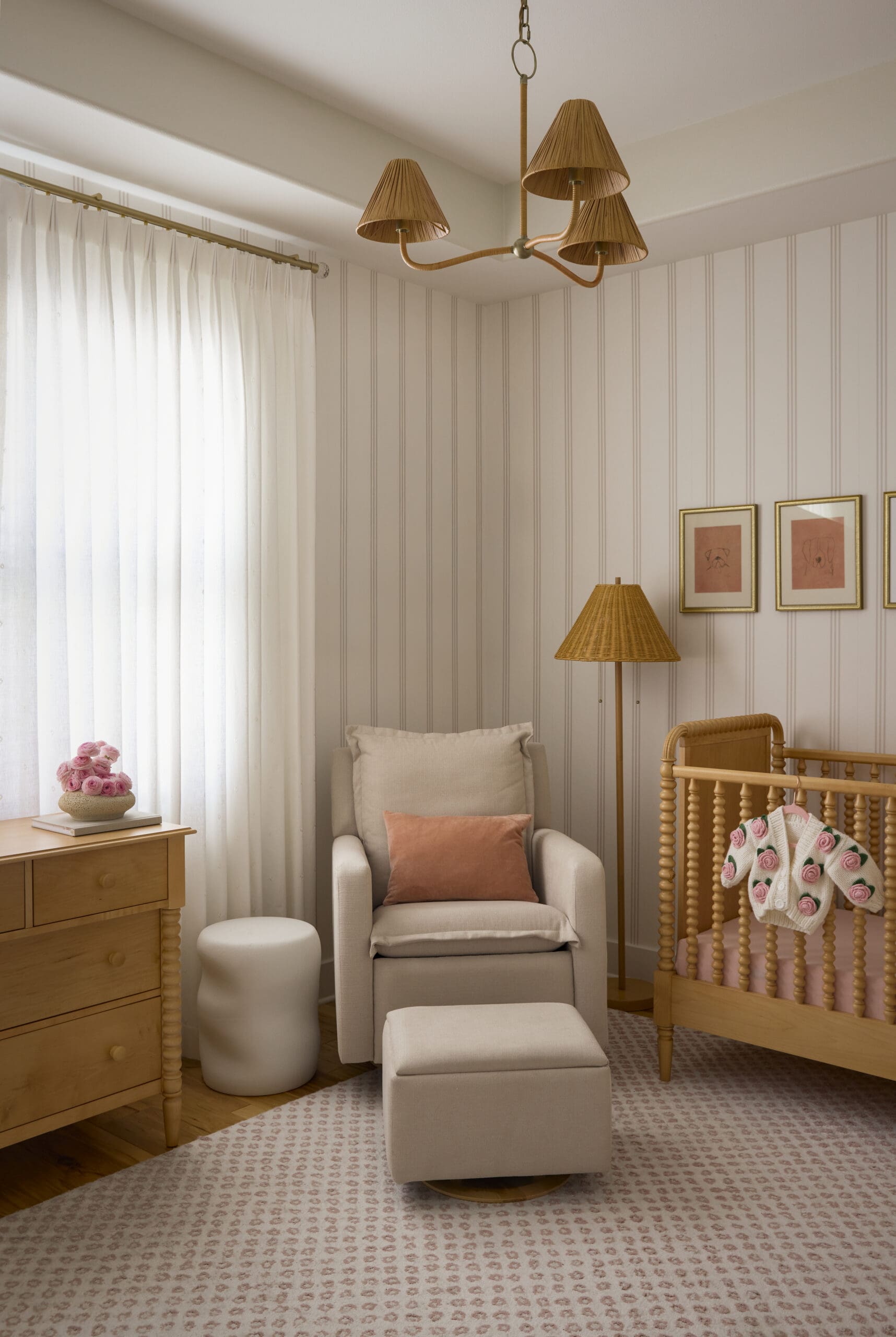 Cozy nursery corner with a beige armchair, pink throw pillow, woven wicker crib, and a wicker floor lamp; pink patterned carpet.