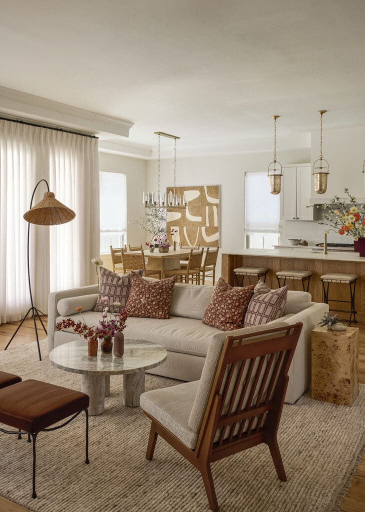 Open-concept living and dining area with a beige sofa, wooden chairs, and marble-topped coffee tables under gold pendant lights.