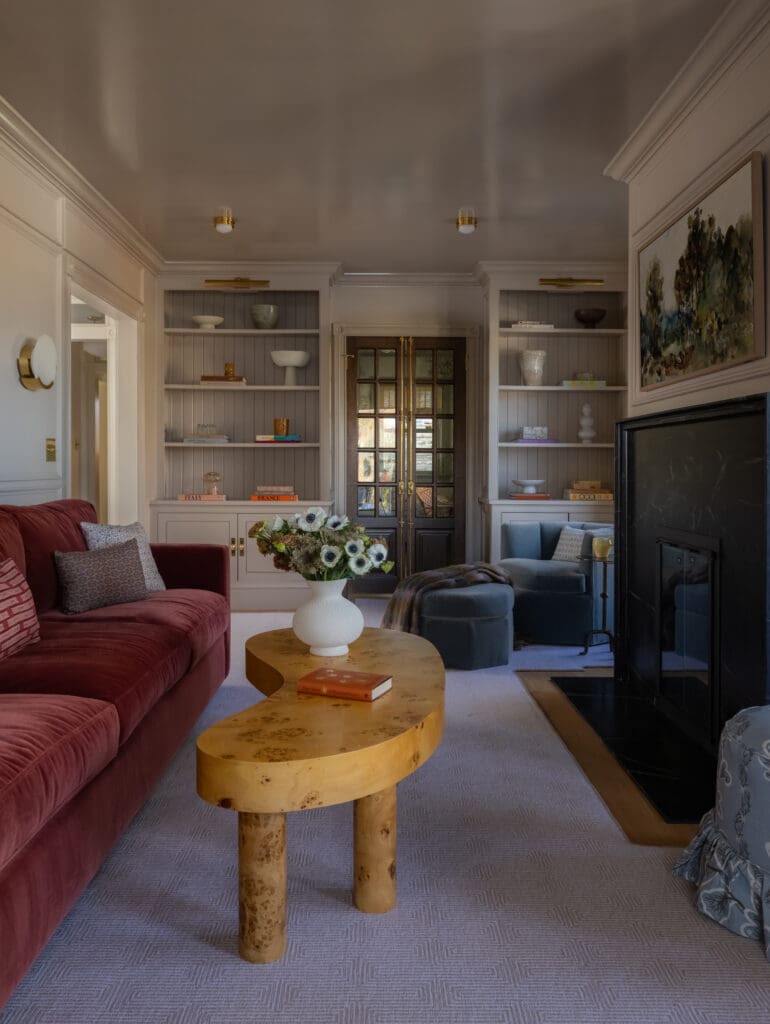 Cozy living room with a red velvet sofa, a curved wooden coffee table, and built-in gray bookshelves flanking a glass-paneled door.