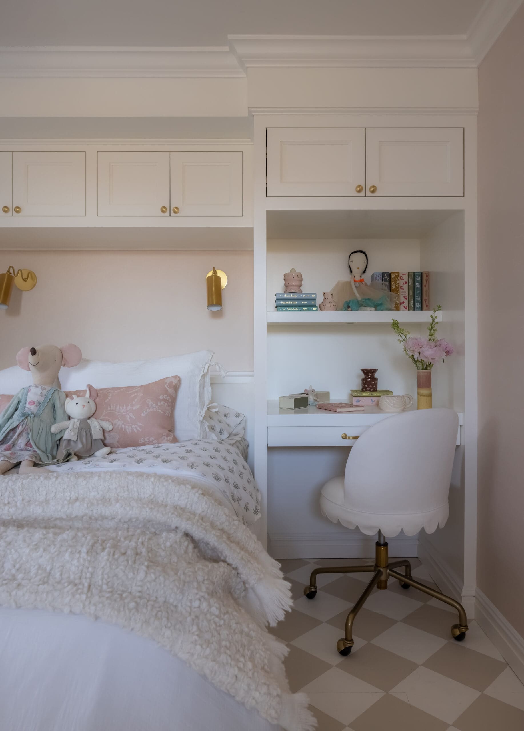 White bedroom with built-in shelves and cabinets, pastel decor, and a fluffy white bedspread adorned with stuffed mice and pink pillows.