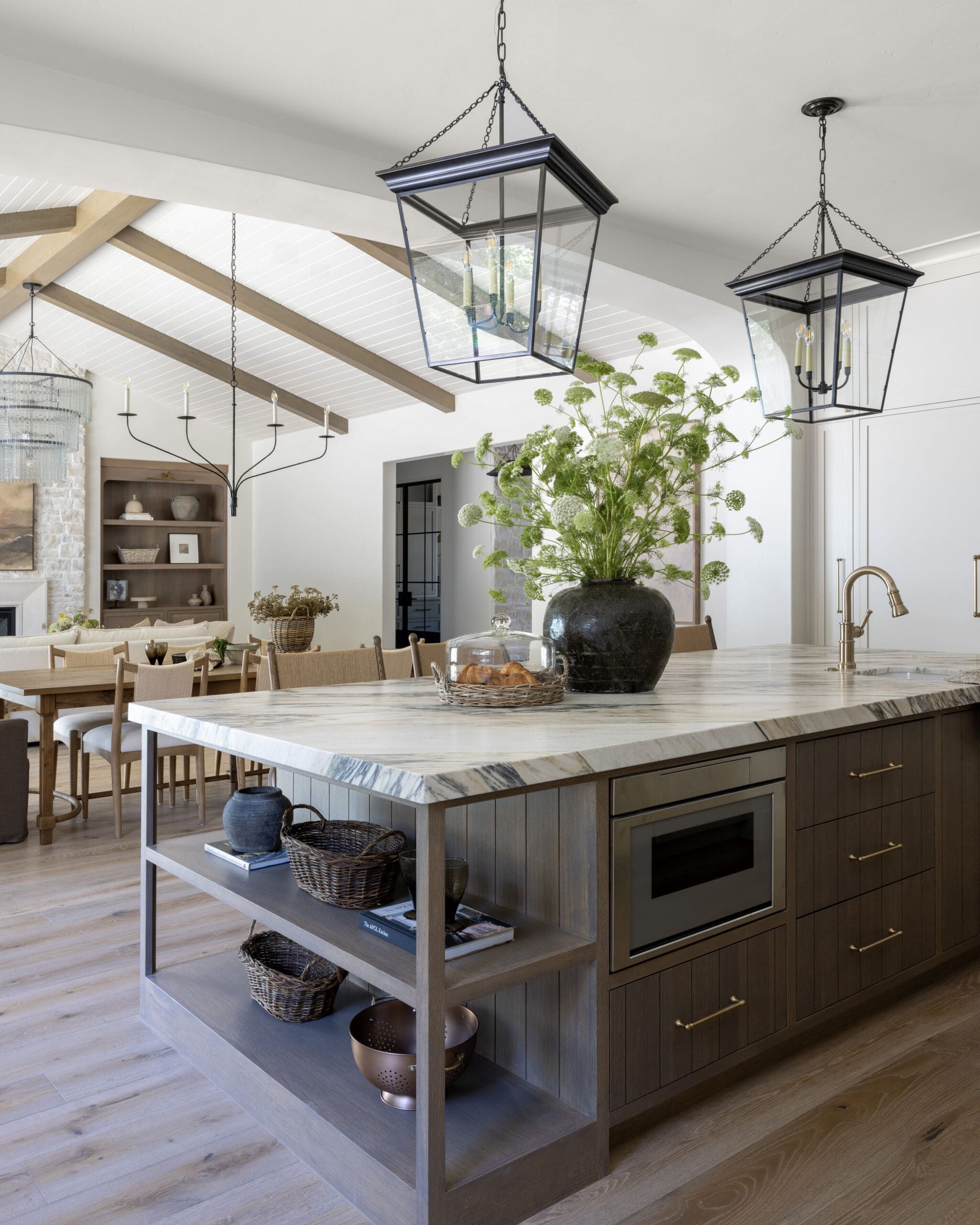 Marble-topped kitchen island with dark wood base and open shelving in a bright open-plan space.