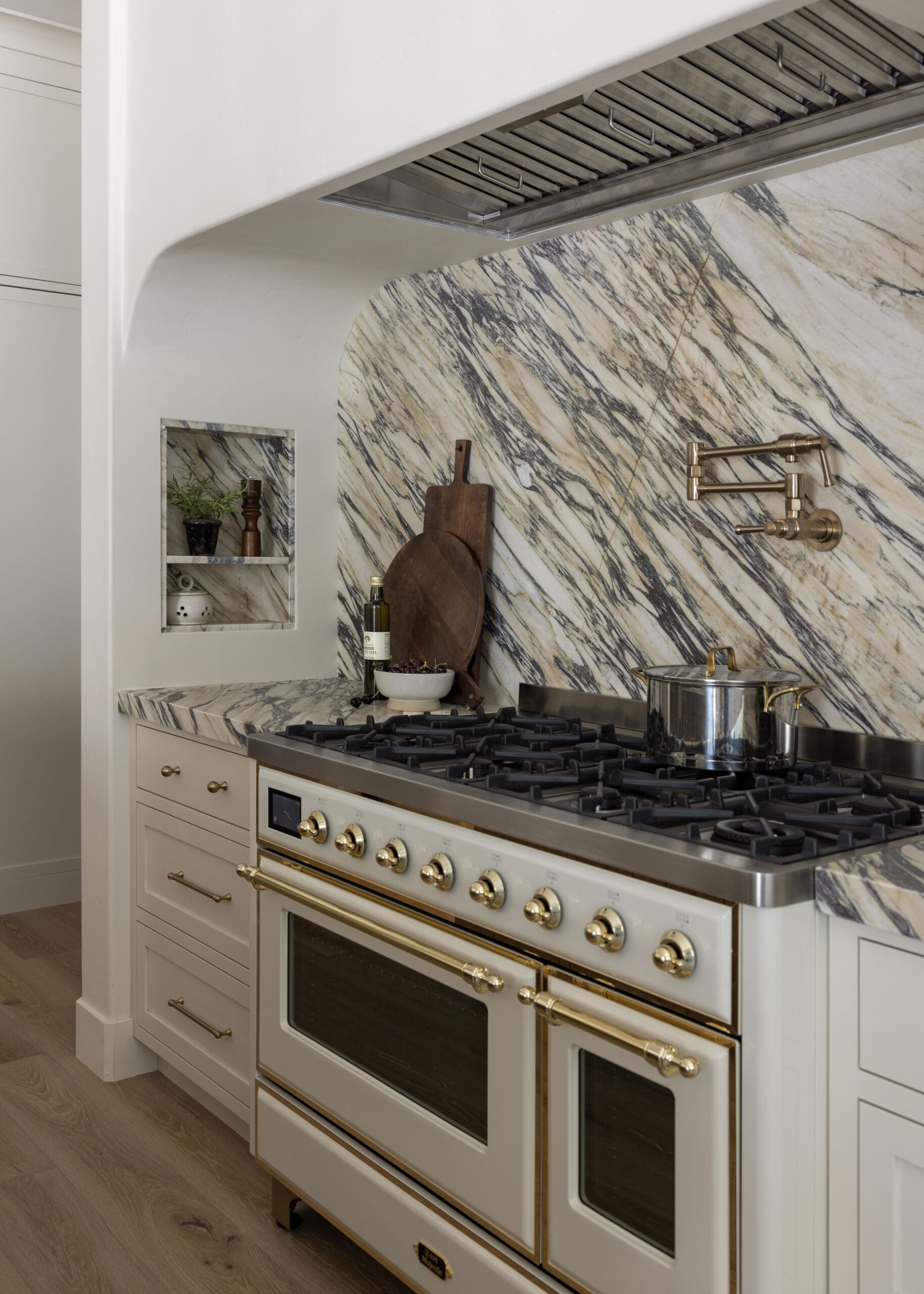 Stainless steel range with brass hardware and a marble backsplash; a pot sits on the stove with cutting boards nearby.