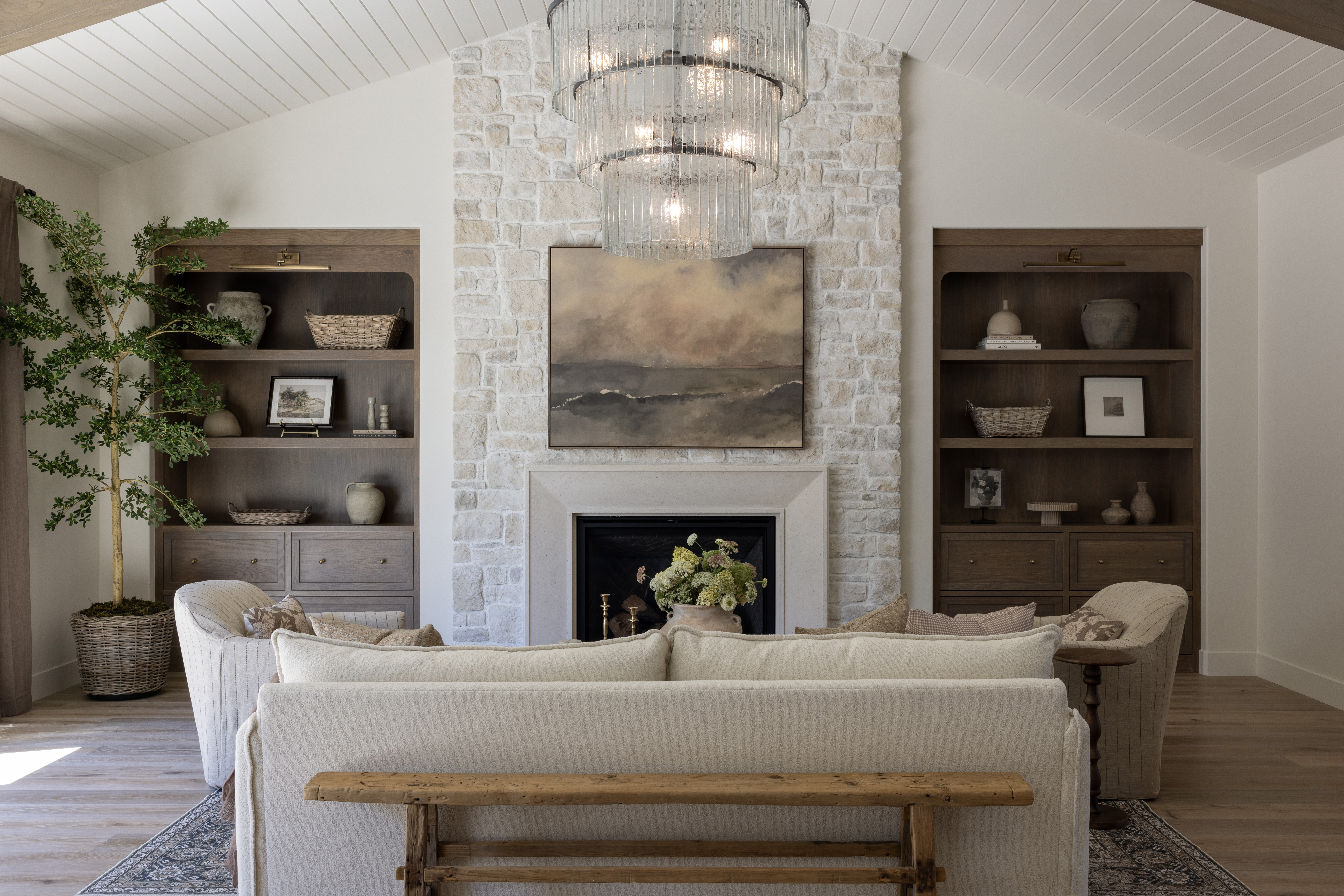 Cozy living room with a stone fireplace, vaulted white paneled ceiling, and a large multi-tier chandelier.