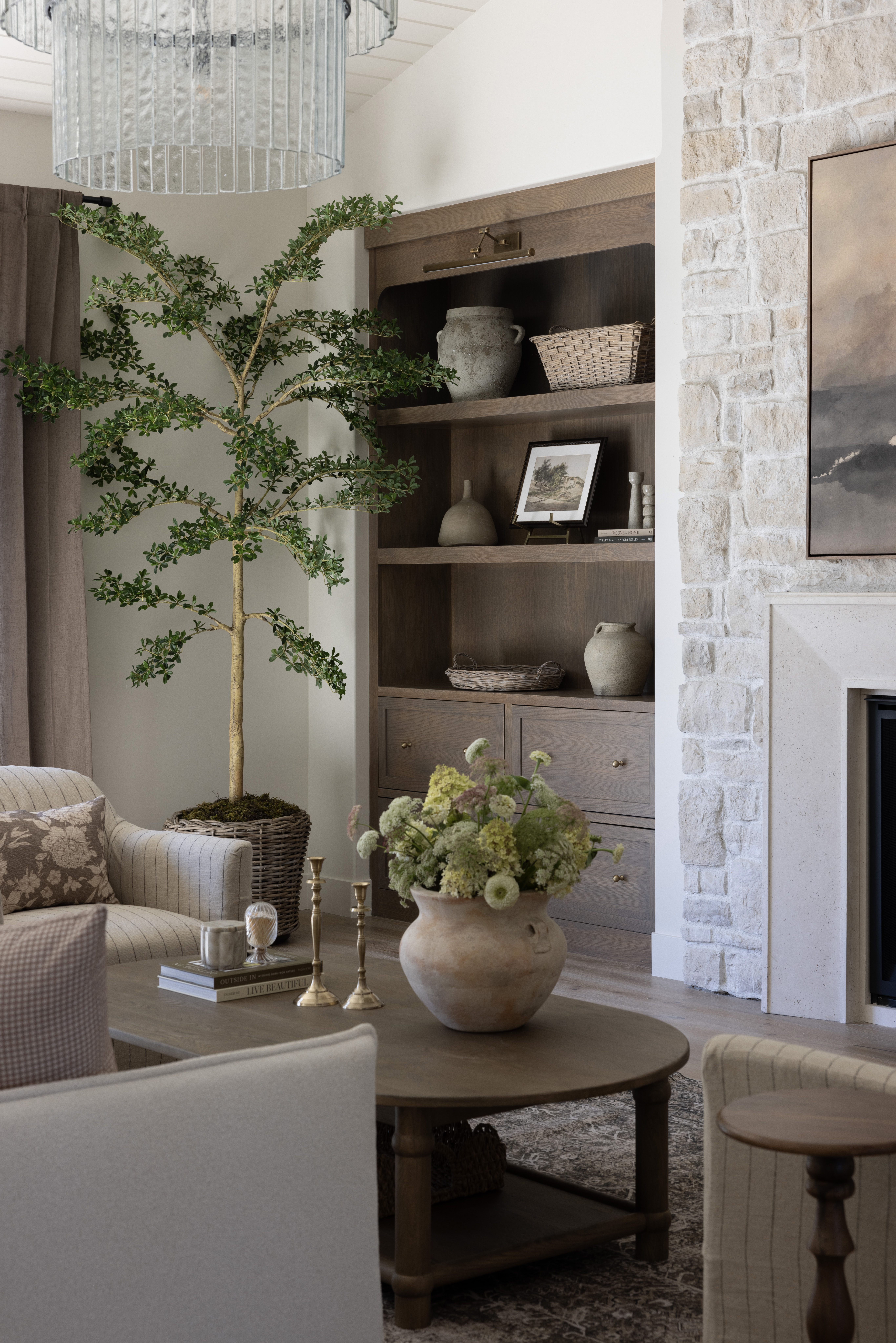 Cozy living room with a stone fireplace, vaulted white paneled ceiling, and a large multi-tier chandelier.