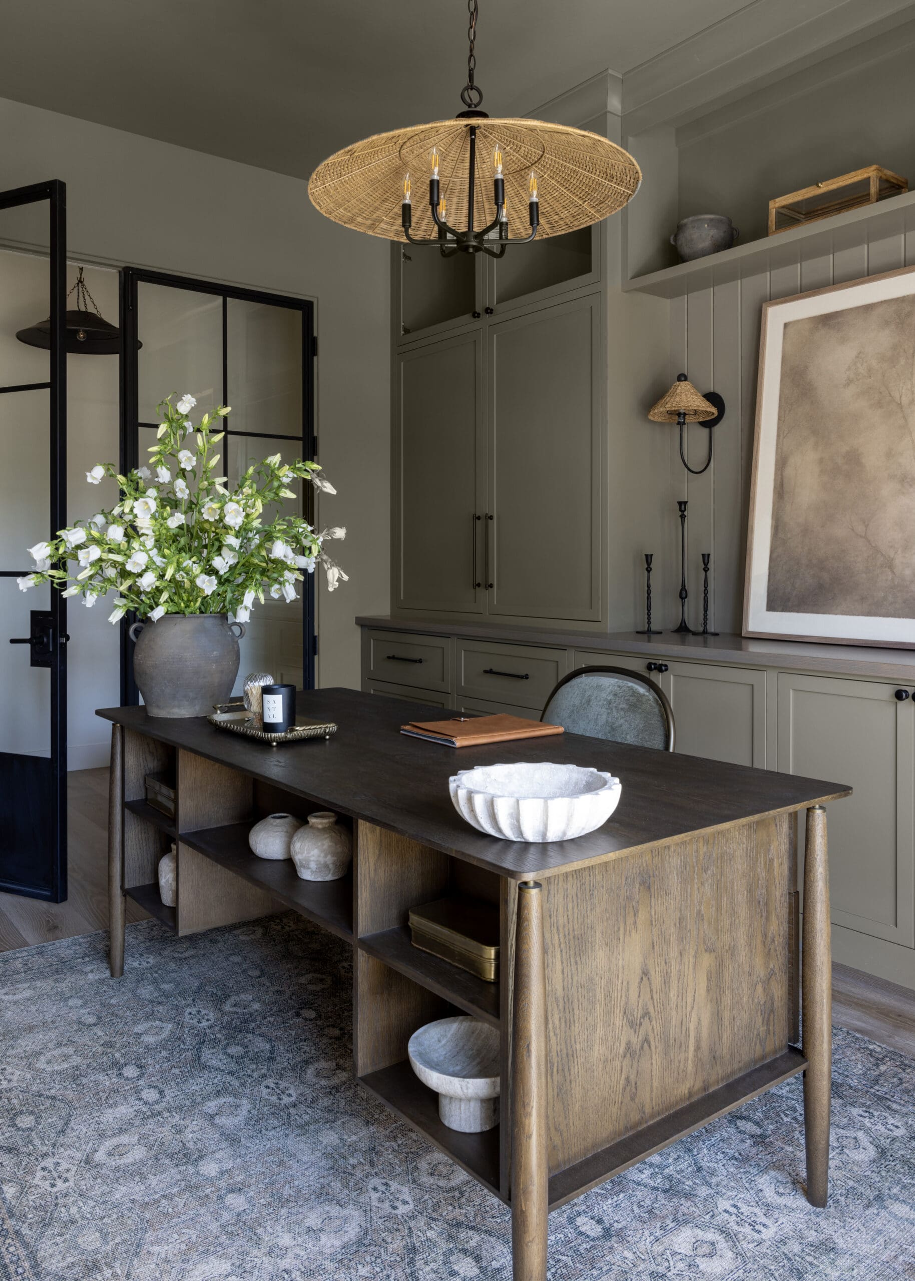 Wood kitchen island with open shelving and a white ceramic bowl on top; gray cabinetry and a woven wicker chandelier above.