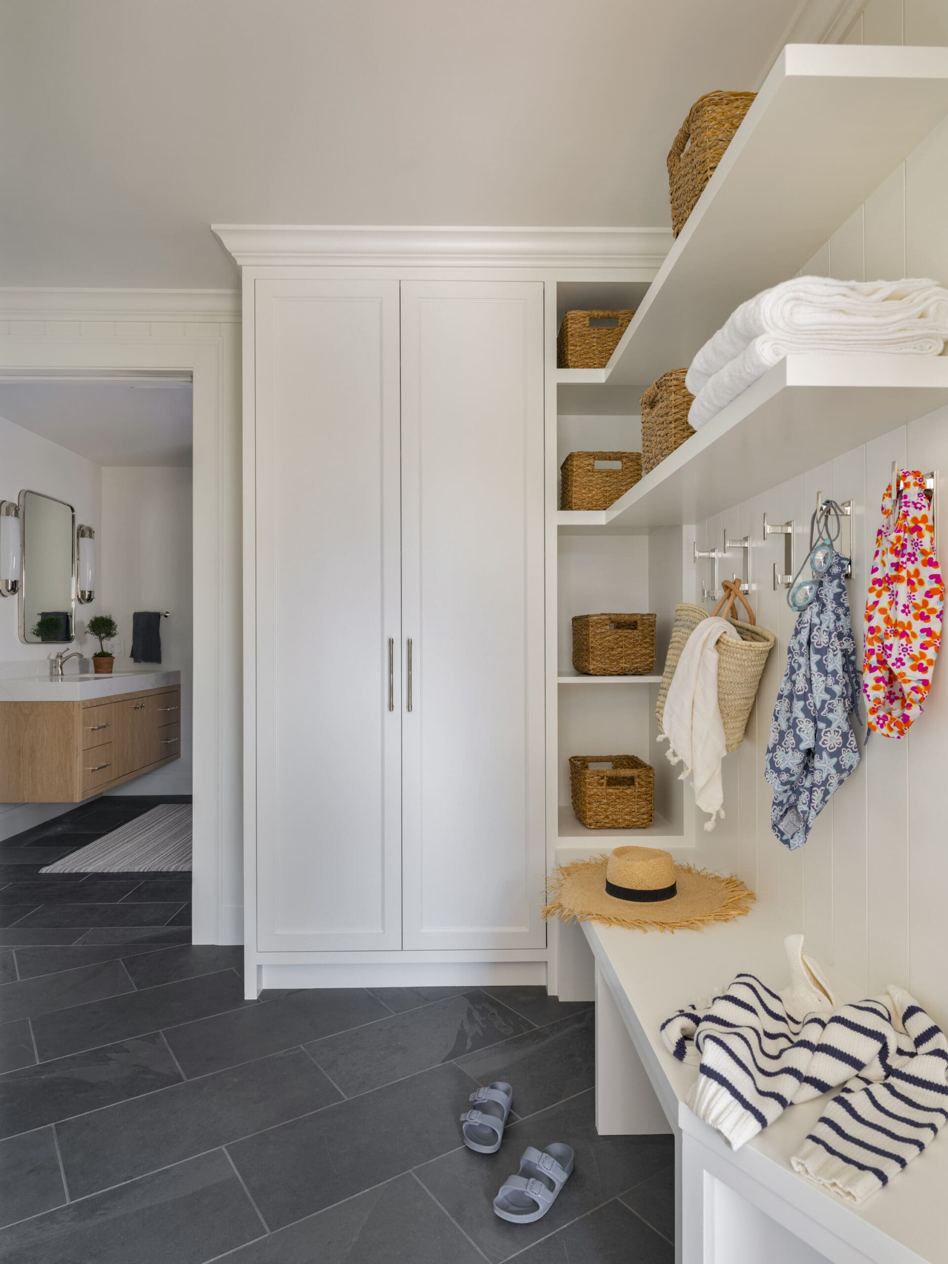 Bright laundry/closet with white cabinetry, open shelves holding wicker baskets and folded towels.