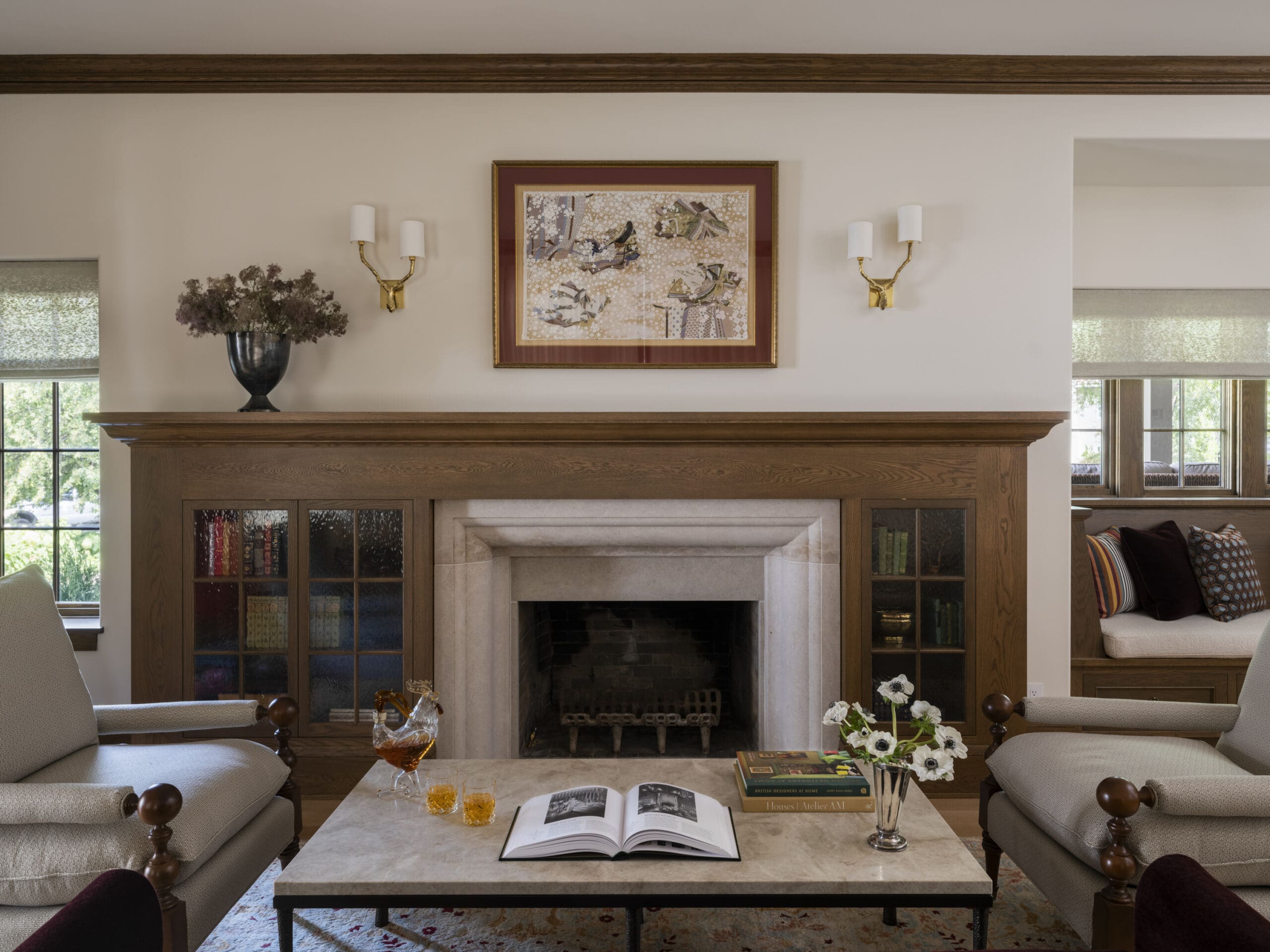 Living room with a wood mantle, framed artwork above the fireplace, and brass wall sconces on either side of the painting.