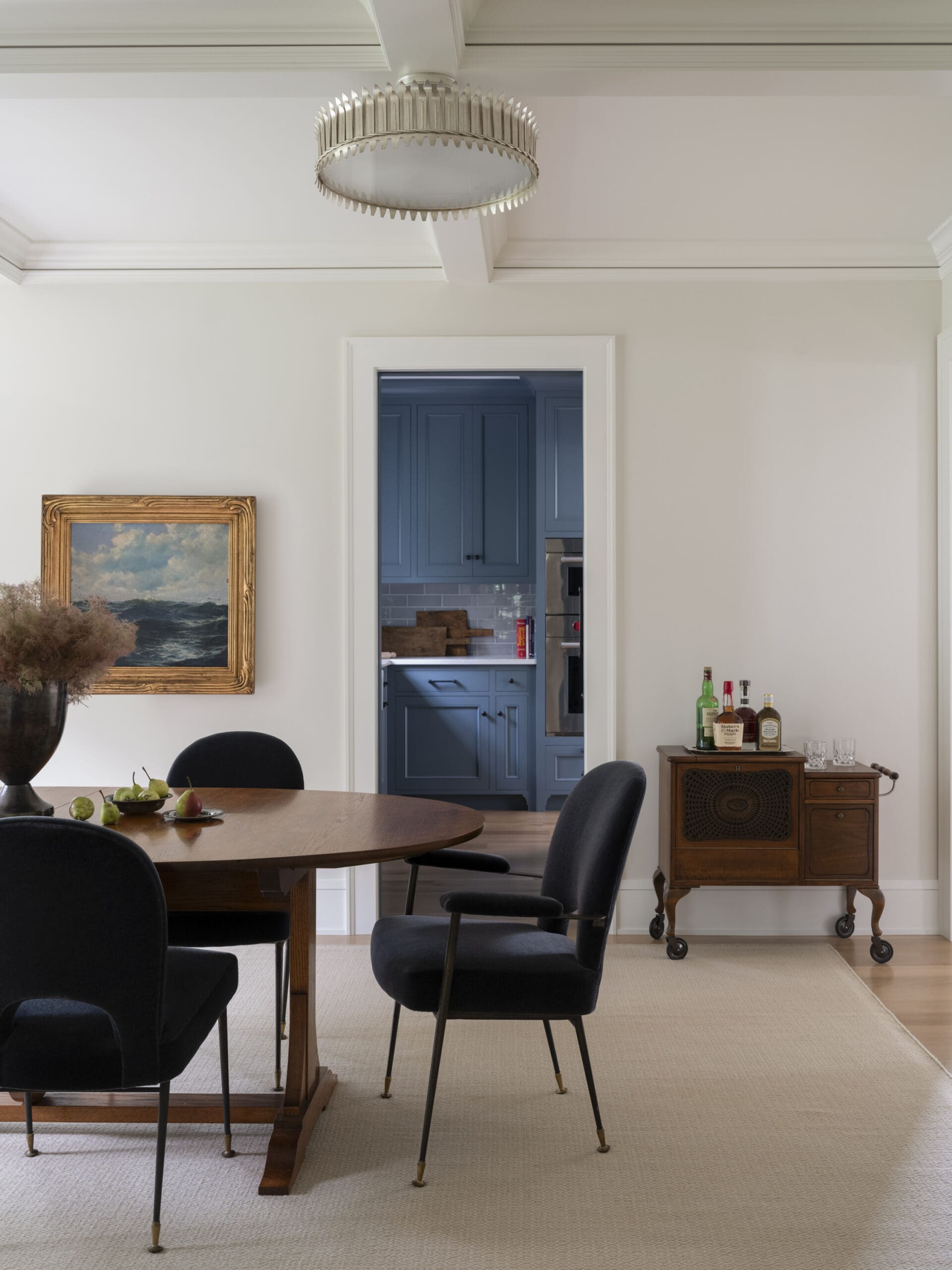 Dining room with a round wooden table, black chairs, and a doorway to a blue kitchen visible in the background.