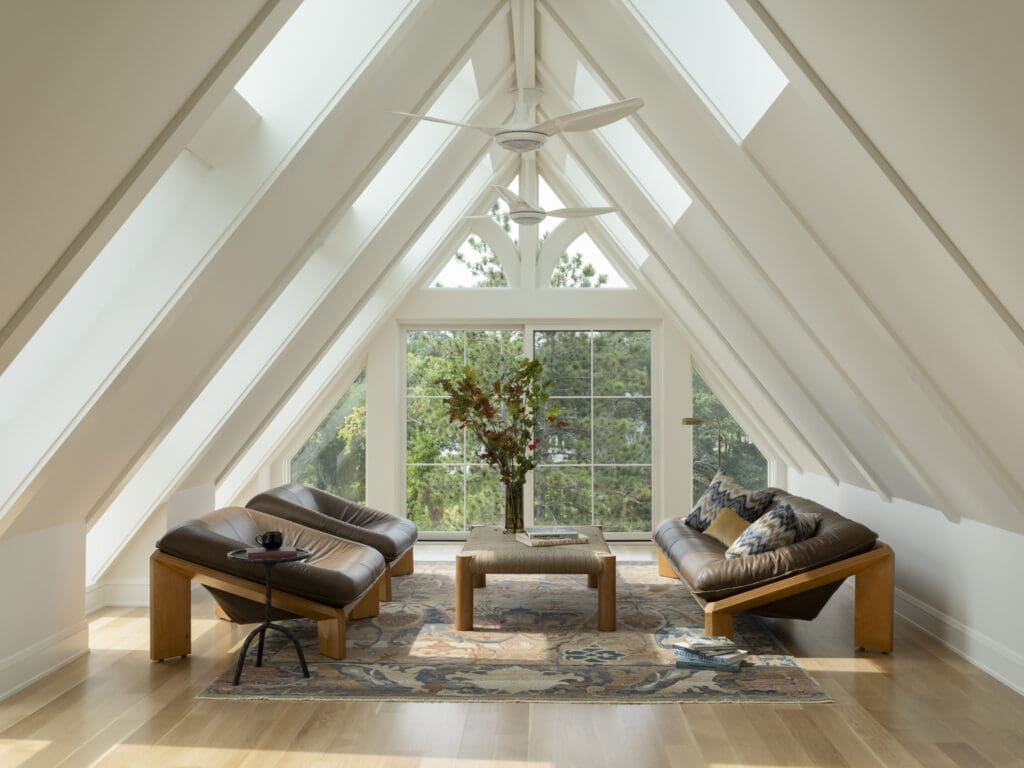 Bright A-frame living room with white walls, large triangular windows, and two brown leather chairs around a wooden coffee table.