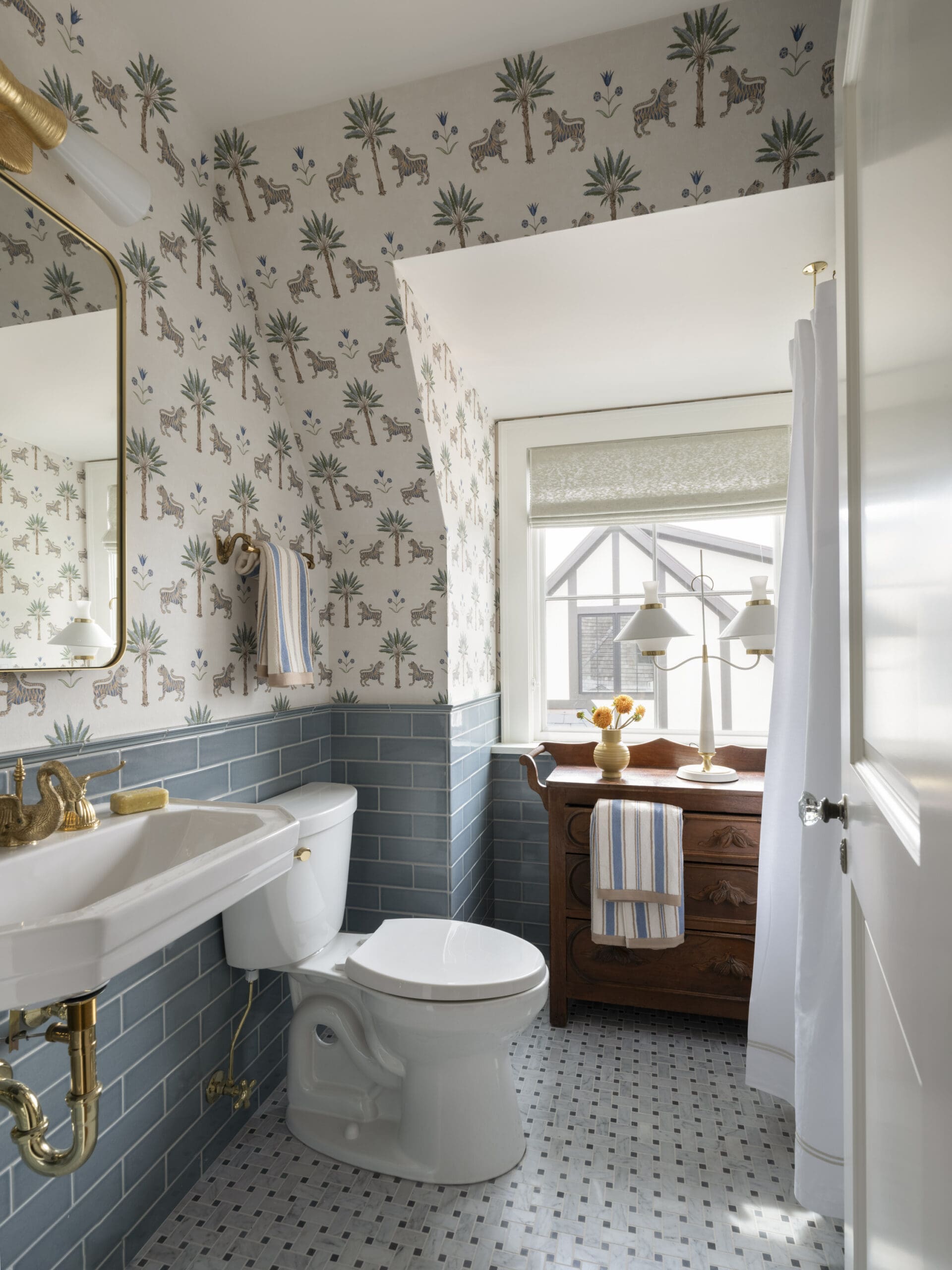 Bathroom with tropical palm and tiger wallpaper, blue tile wainscoting, and white fixtures (toilet and sink).