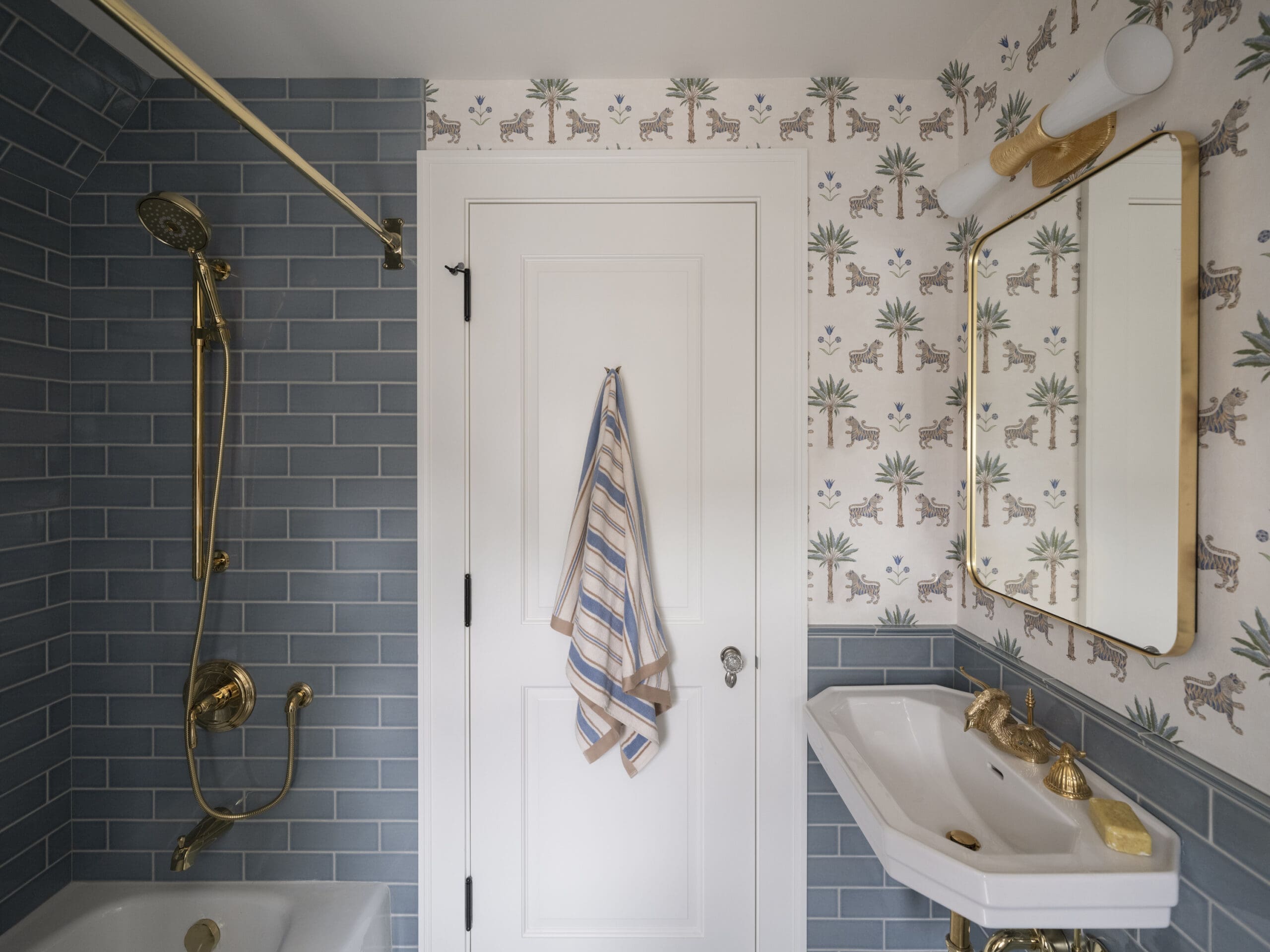 Bathroom interior with blue tiled shower area on the left, white paneled door in the center, and gold fixtures and towel hanging nearby.