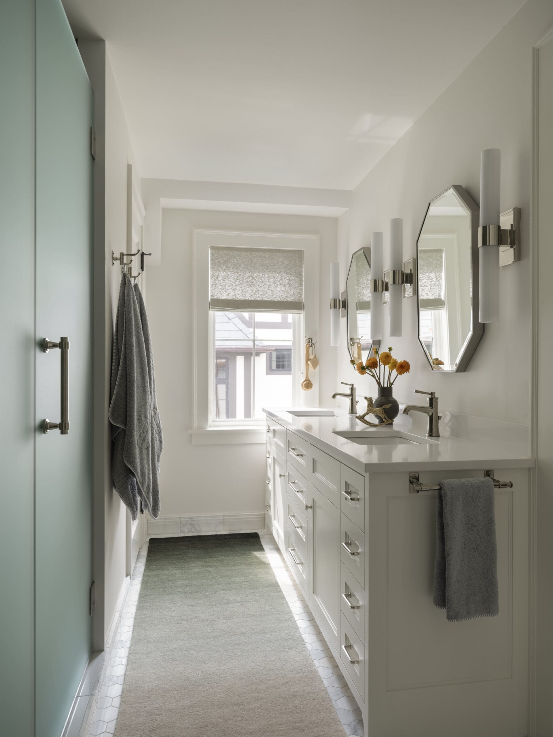 Bright modern bathroom with a white double vanity, chrome faucets, and mirrored wall lamps along the right wall.