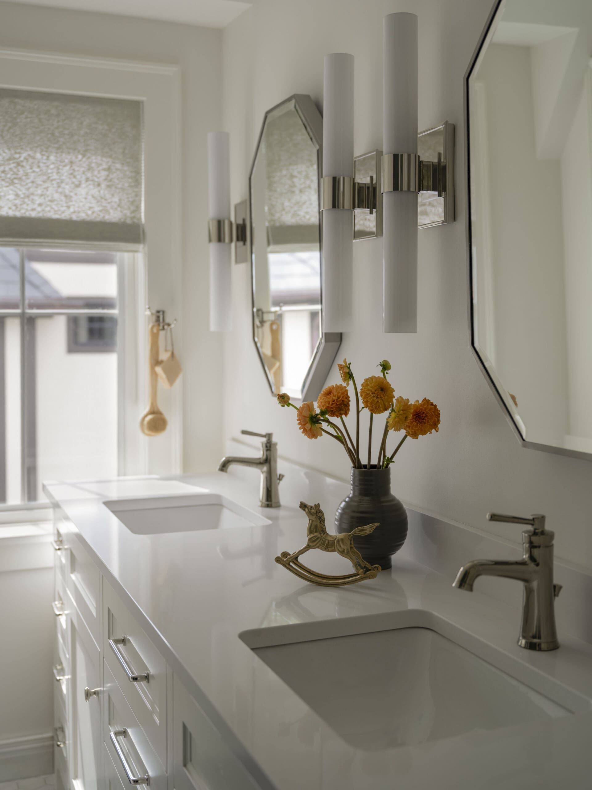 Double-sink white bathroom vanity with chrome faucets and a vase of orange flowers on the counter