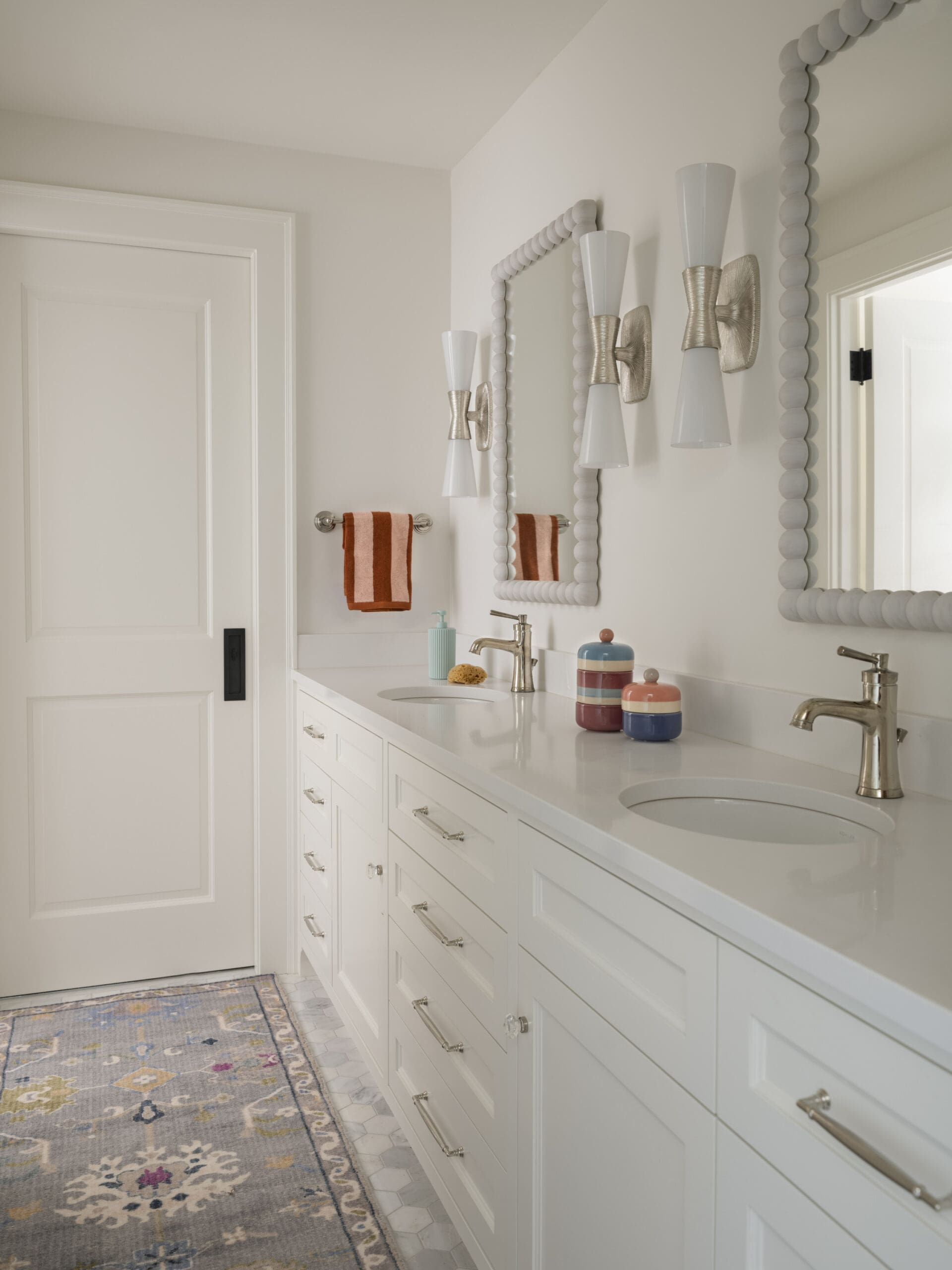 Bright bathroom with a white double-sink vanity, gold faucets, bubble-frame mirrors, and matching sconces.