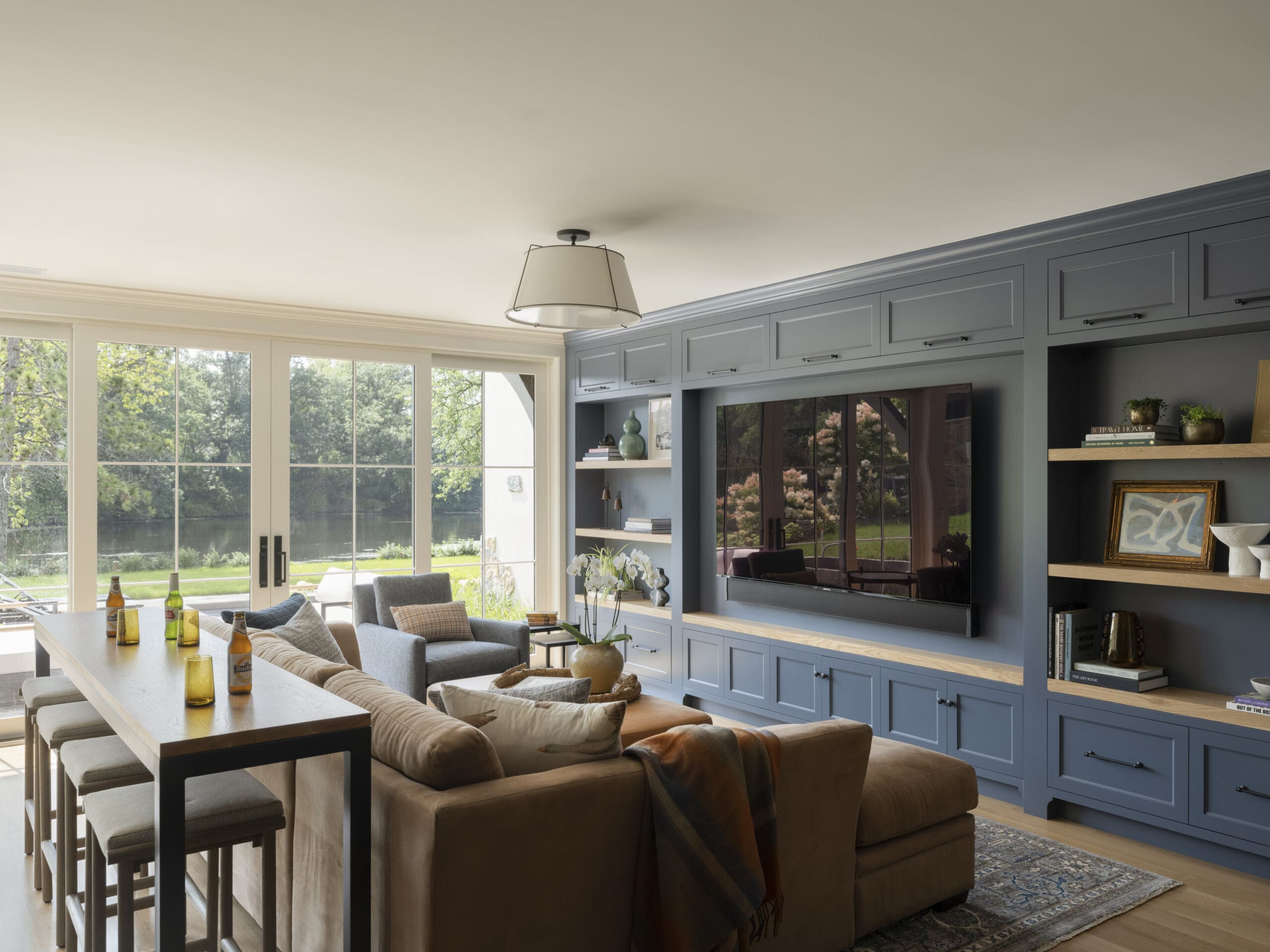 Open-plan living area with blue-gray cabinetry, a long island, and a beige sofa by large windows.